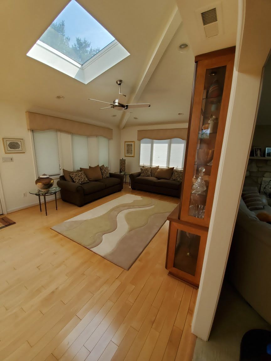 Bright living room with skylight, wood floors, dark sofas, and a beige patterned rug
