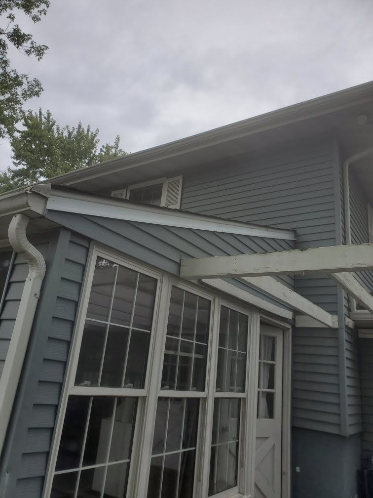 Gray house exterior with windows, small awning, and roof gutter under a cloudy sky