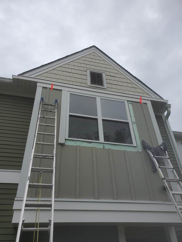 Two ladders leaning against a gray house below a second-story window and gable vent
