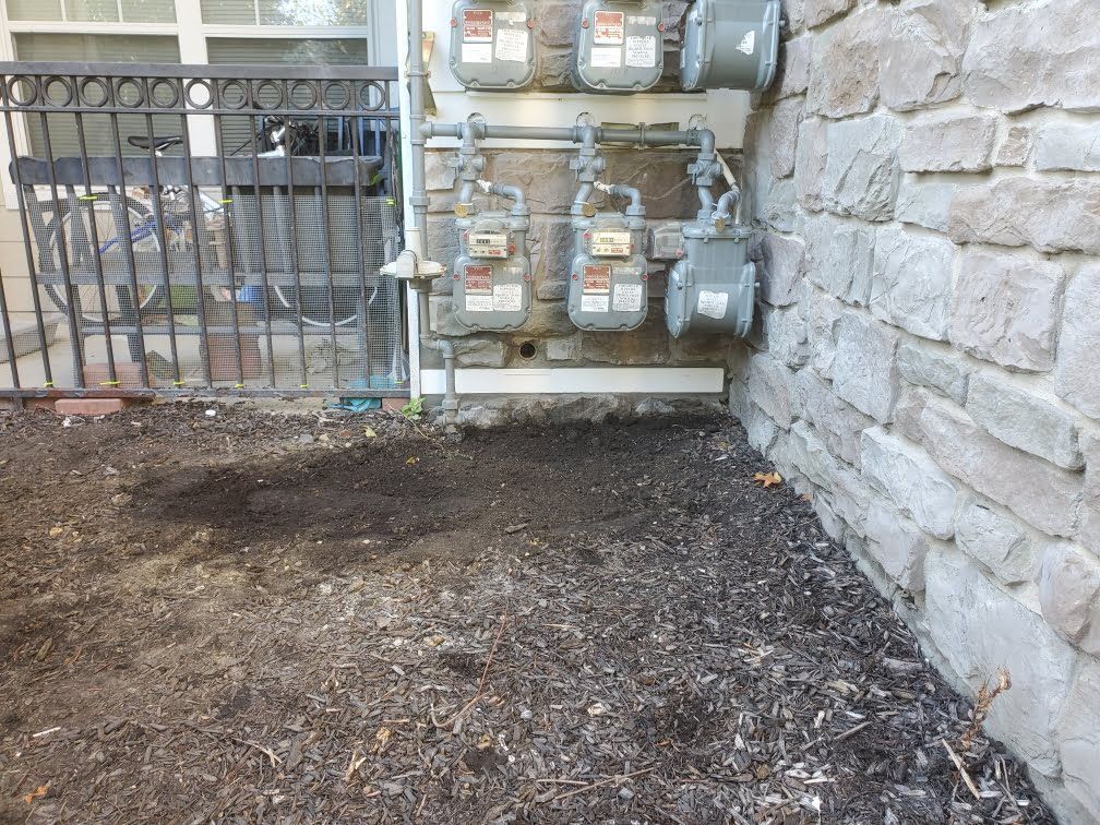 Utility meters on a stone wall beside a dirt patch and metal fence near an outdoor area