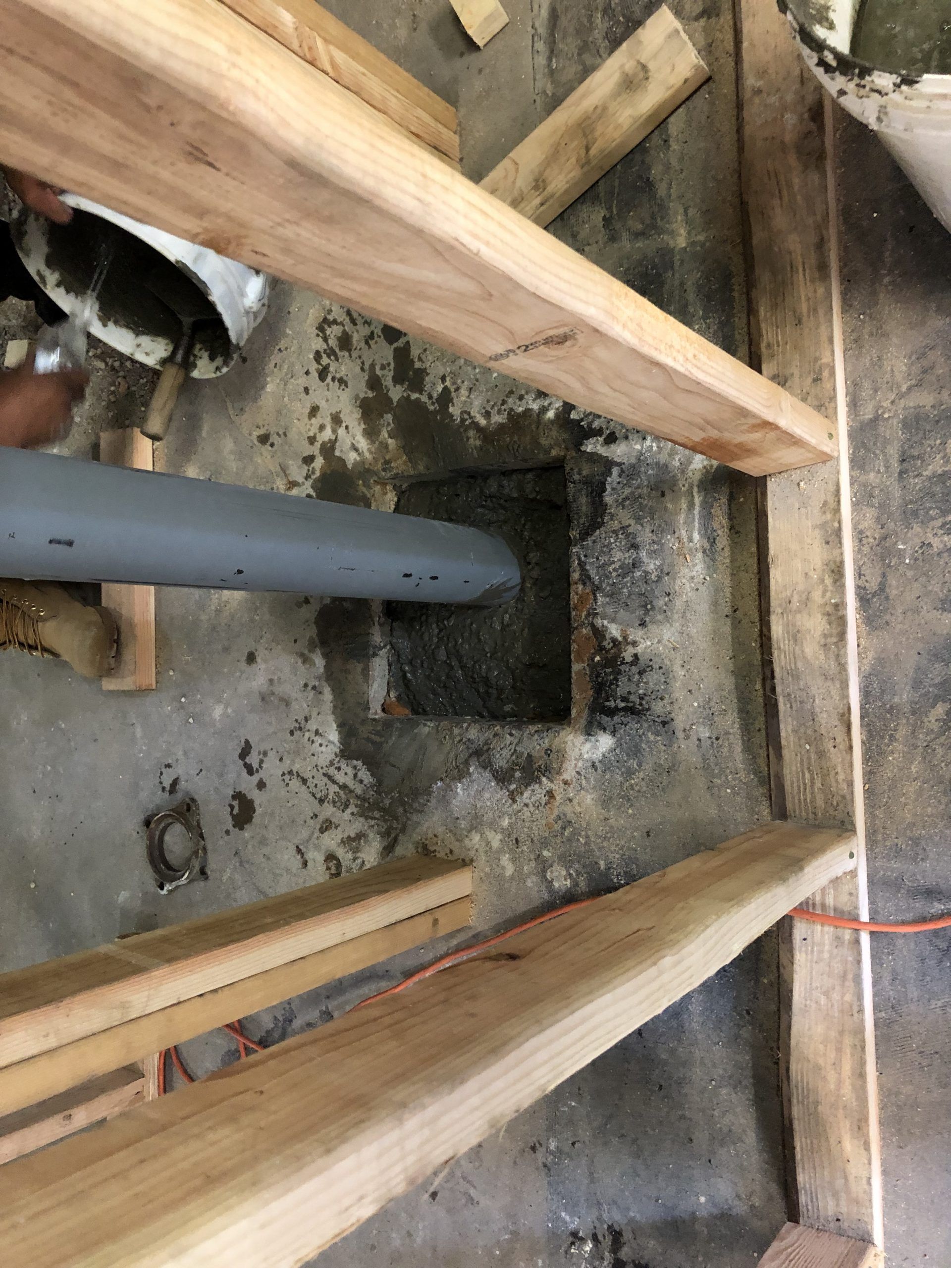Construction framing around a concrete floor with a gray pipe passing through the center.