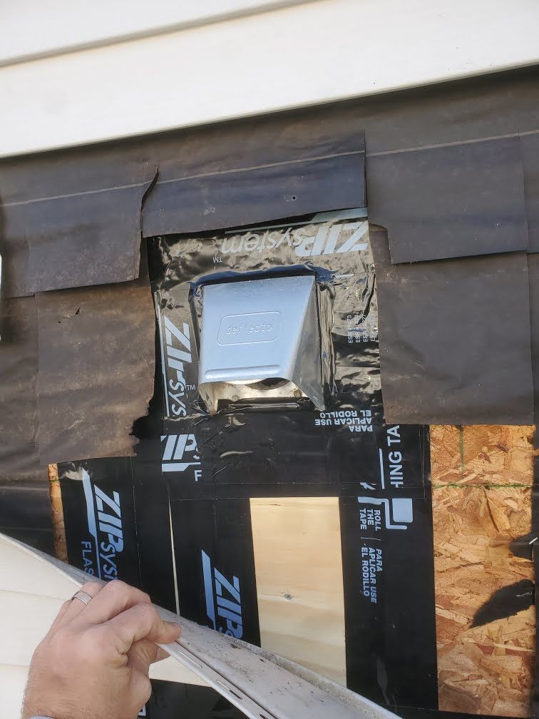 Hand placing black flashing around a small roof vent in a shingled roof repair area