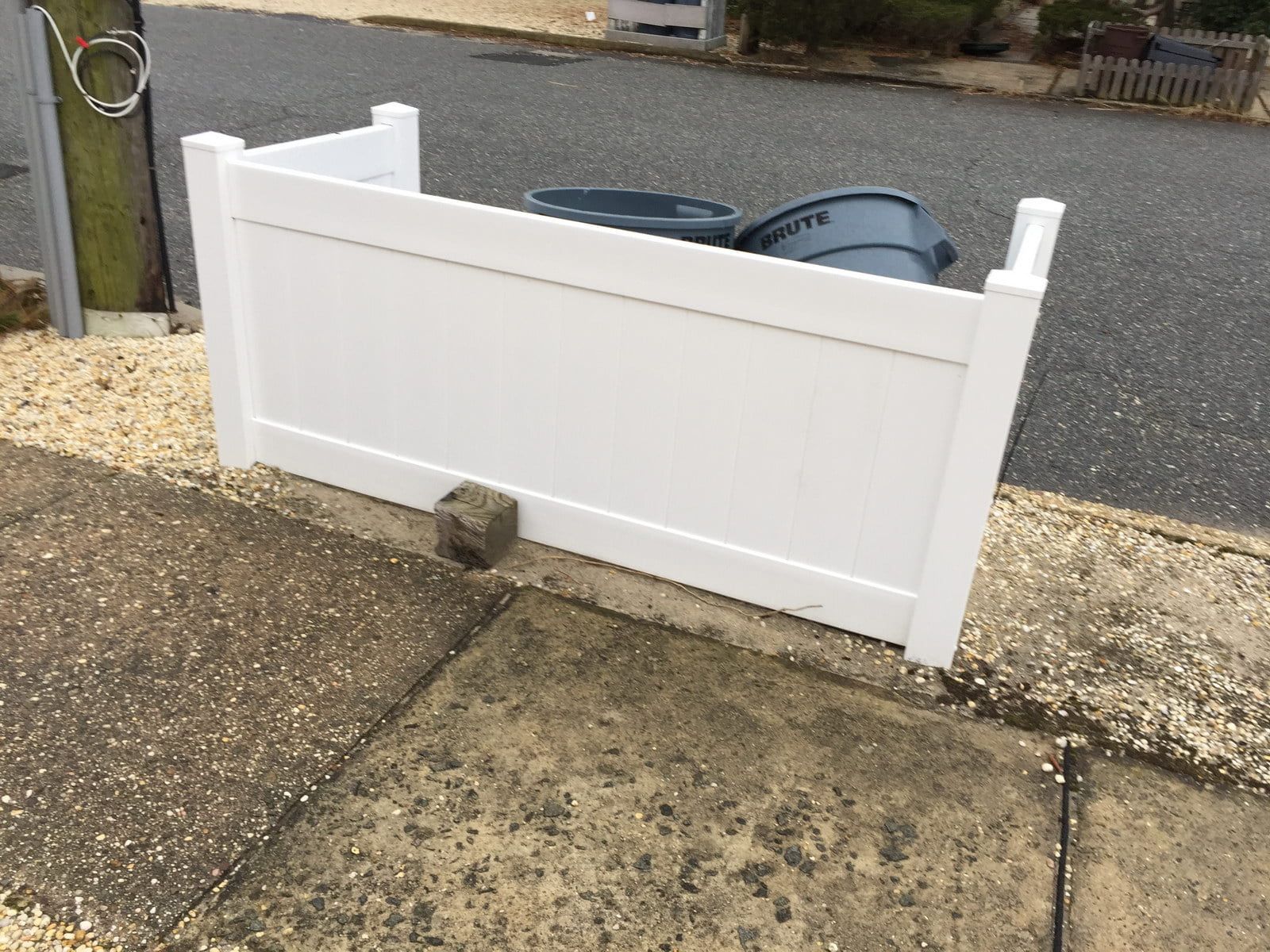 White driveway gate beside a gravel-lined street, with a gray car visible behind it.