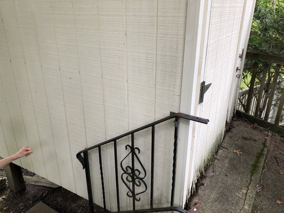 Exterior wall with black railing and small staircase beside a white building; a hand reaches in from left.