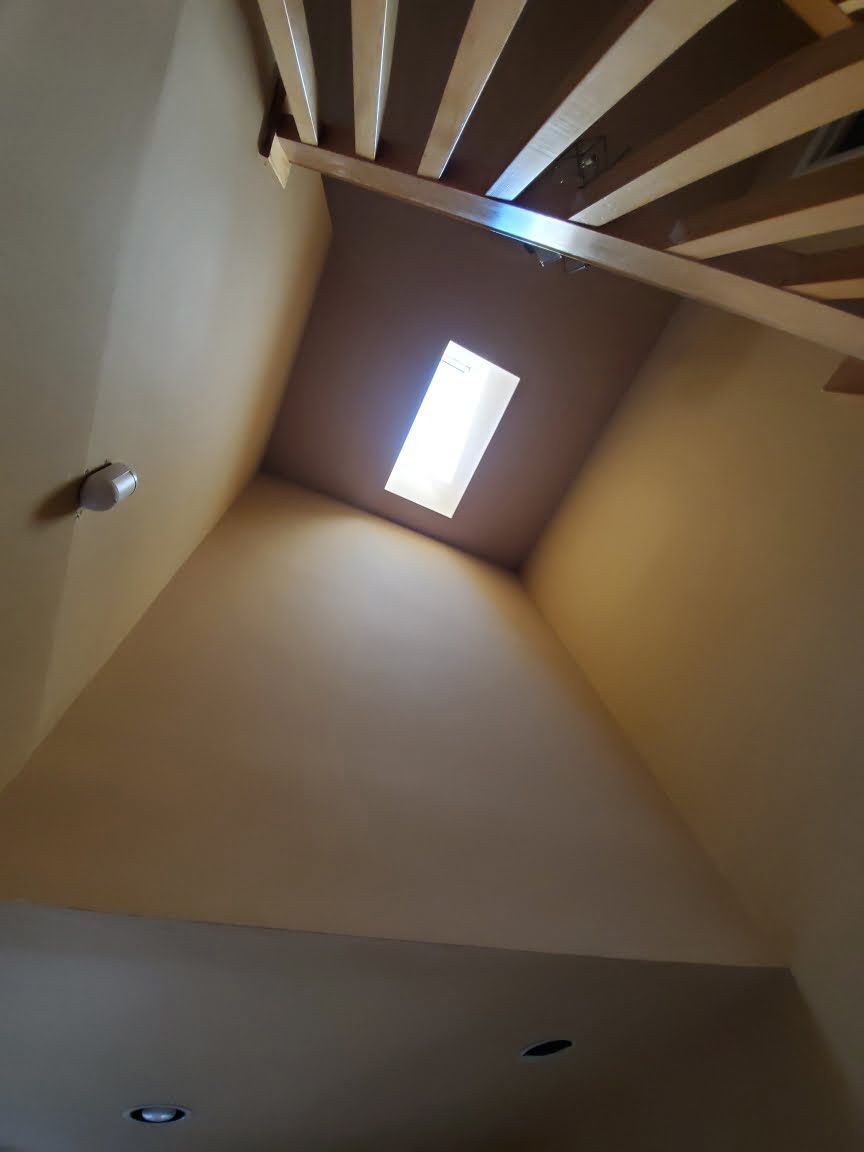 Looking up a stairwell with a skylight, beige walls, and exposed ceiling beams.