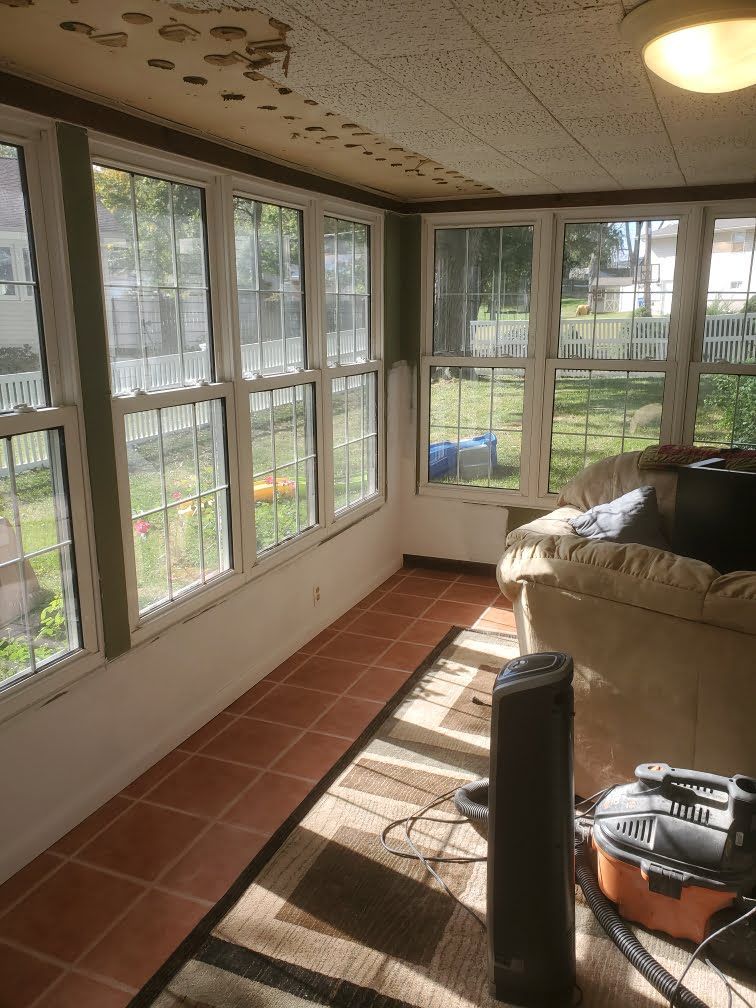 Sunroom with large windows, terracotta tile floor, beige couch, and scattered tools in bright daylight