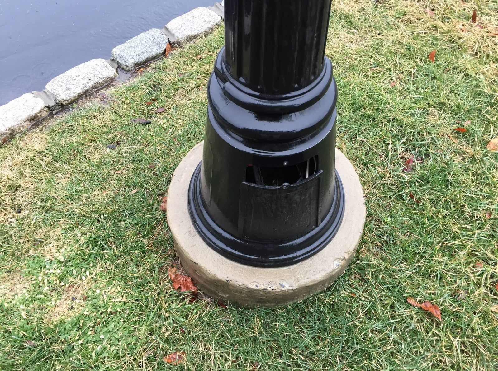 Black lamppost base on grass beside a stone curb in a park.