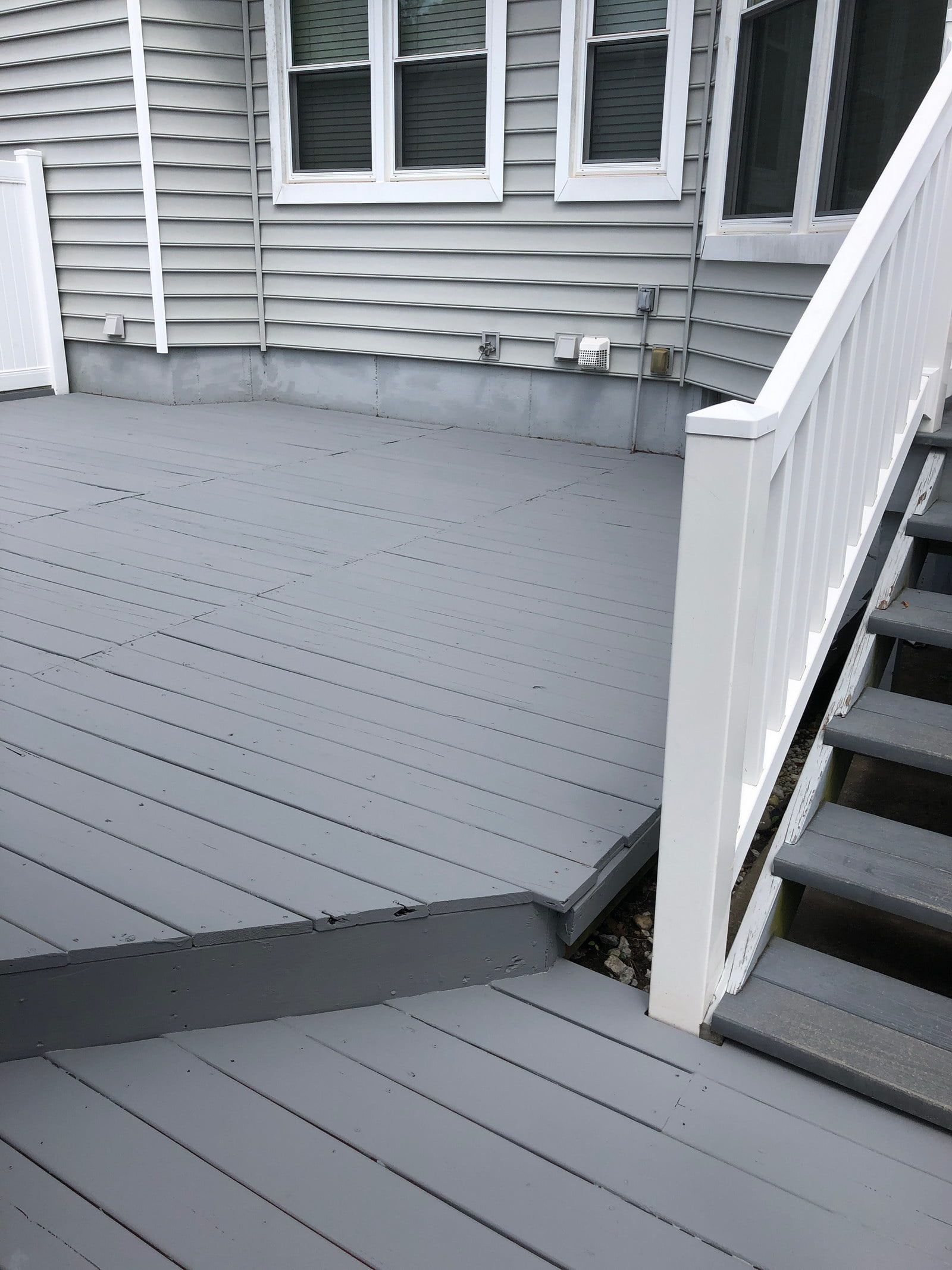 Gray deck with white railing and stairs beside a house exterior.