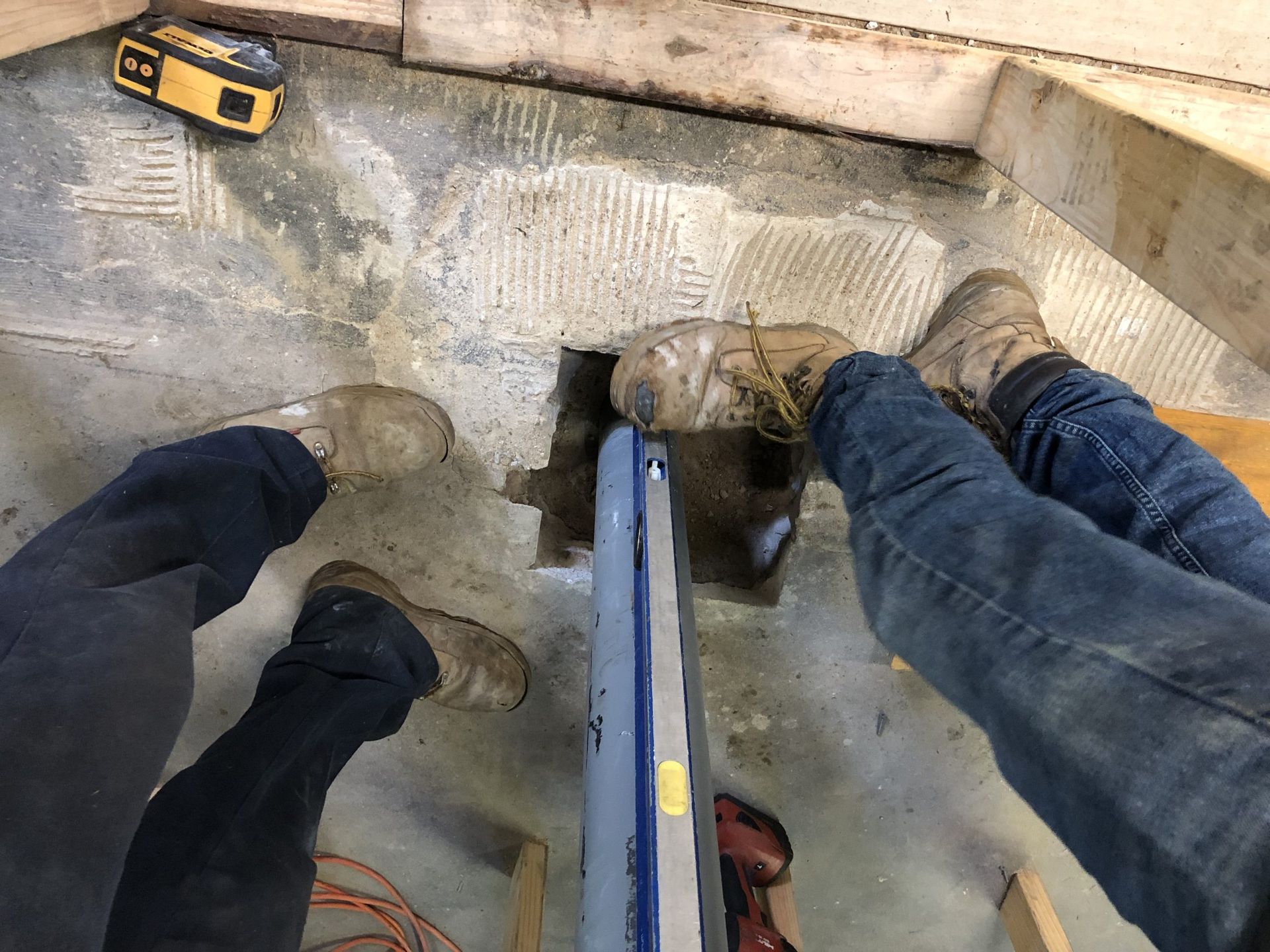 Three workers’ boots and a yellow tool inside a concrete pit or trench