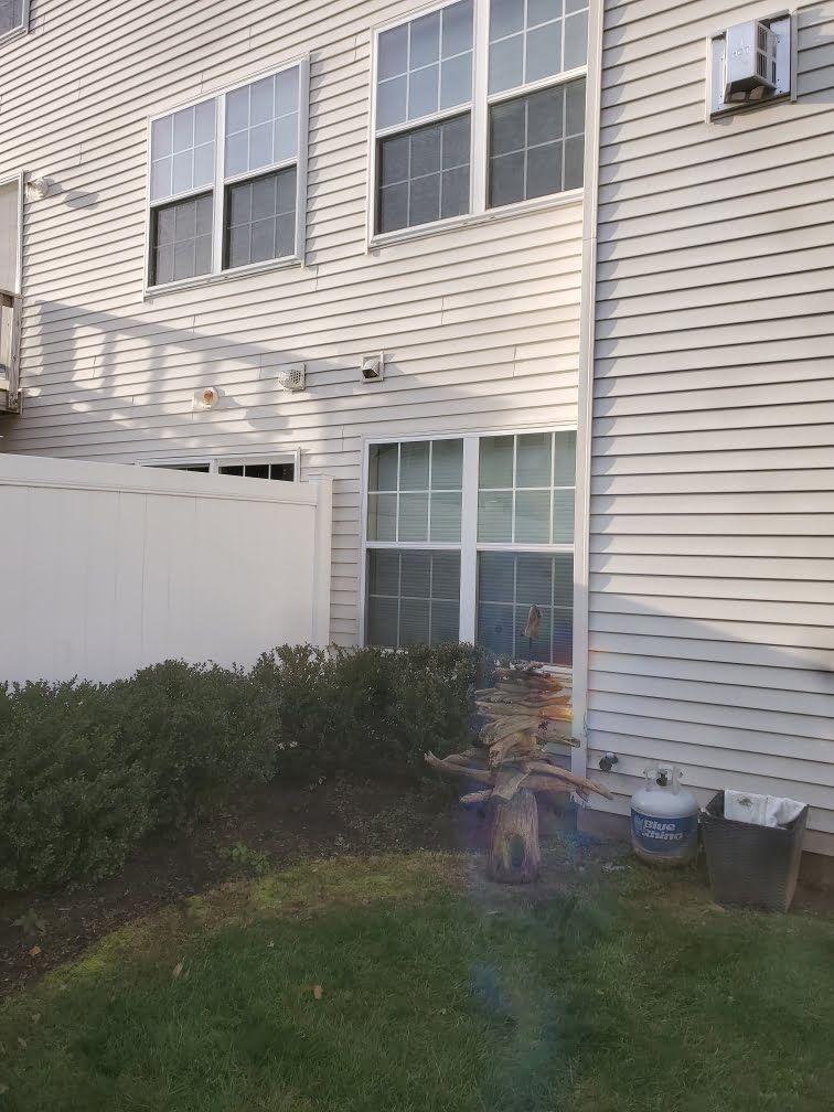 Backyard beside a beige townhouse with sliding glass door, white fence, shrubs, and patio items
