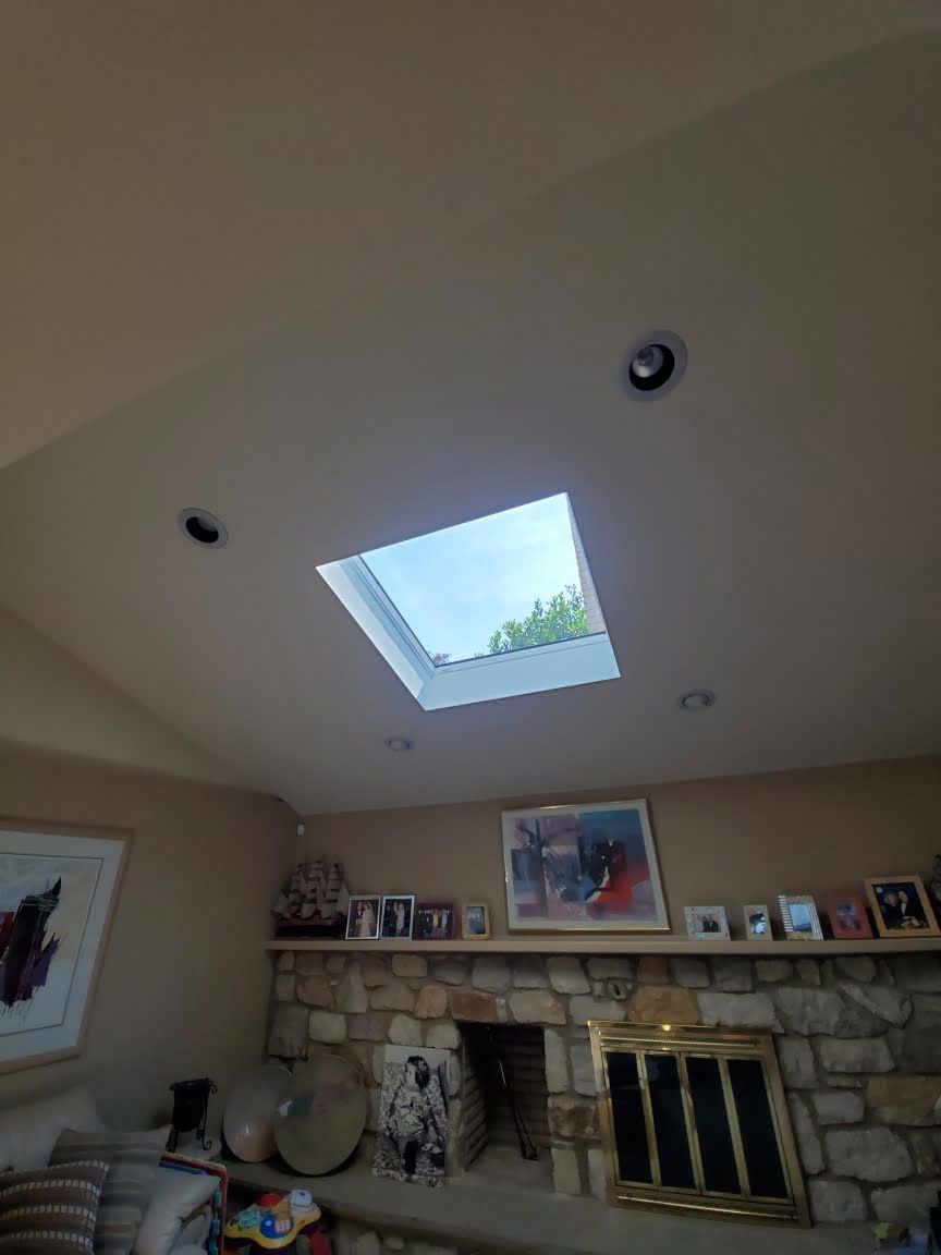 Living room ceiling with skylight, recessed lights, and stone fireplace below with framed art.
