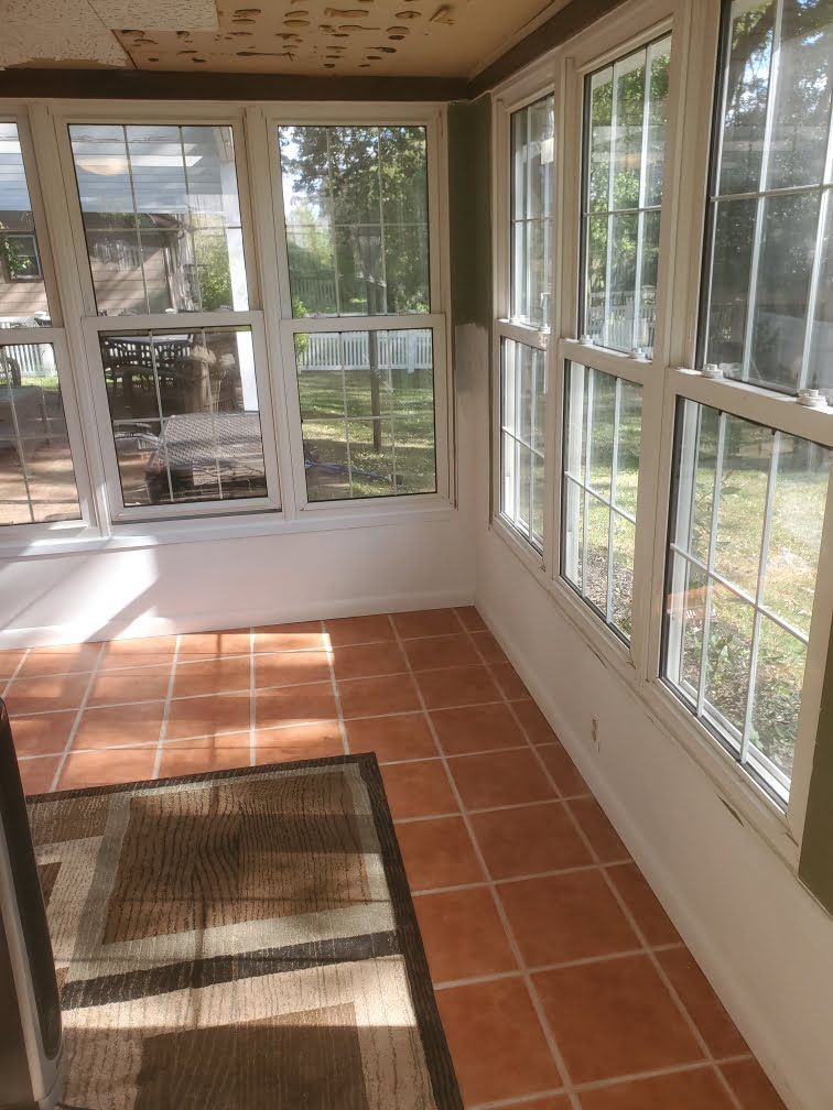 Sunroom with terracotta tile floor, white walls, and large windows looking onto a grassy yard.