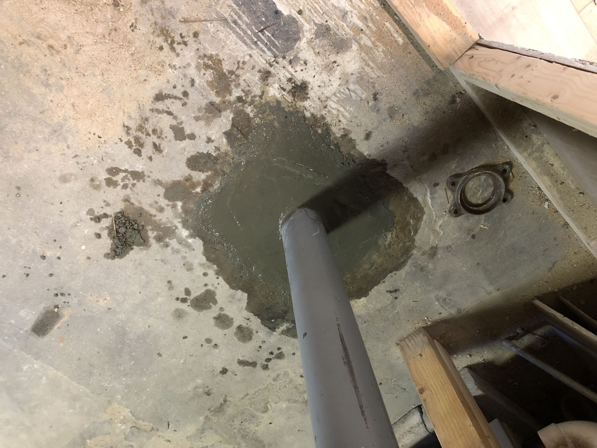 Wet concrete floor with a dark stain around a gray pipe near a wall opening