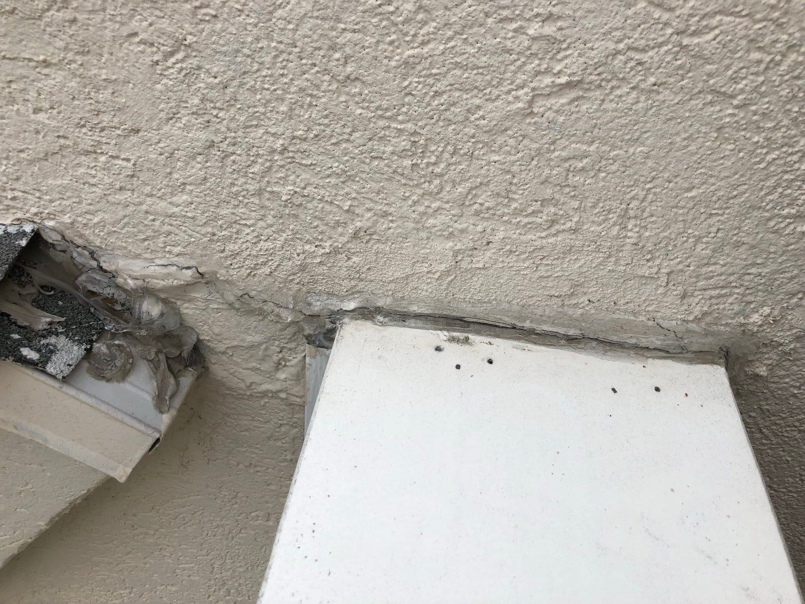 Damaged stucco wall with a broken opening and a white board leaning below it
