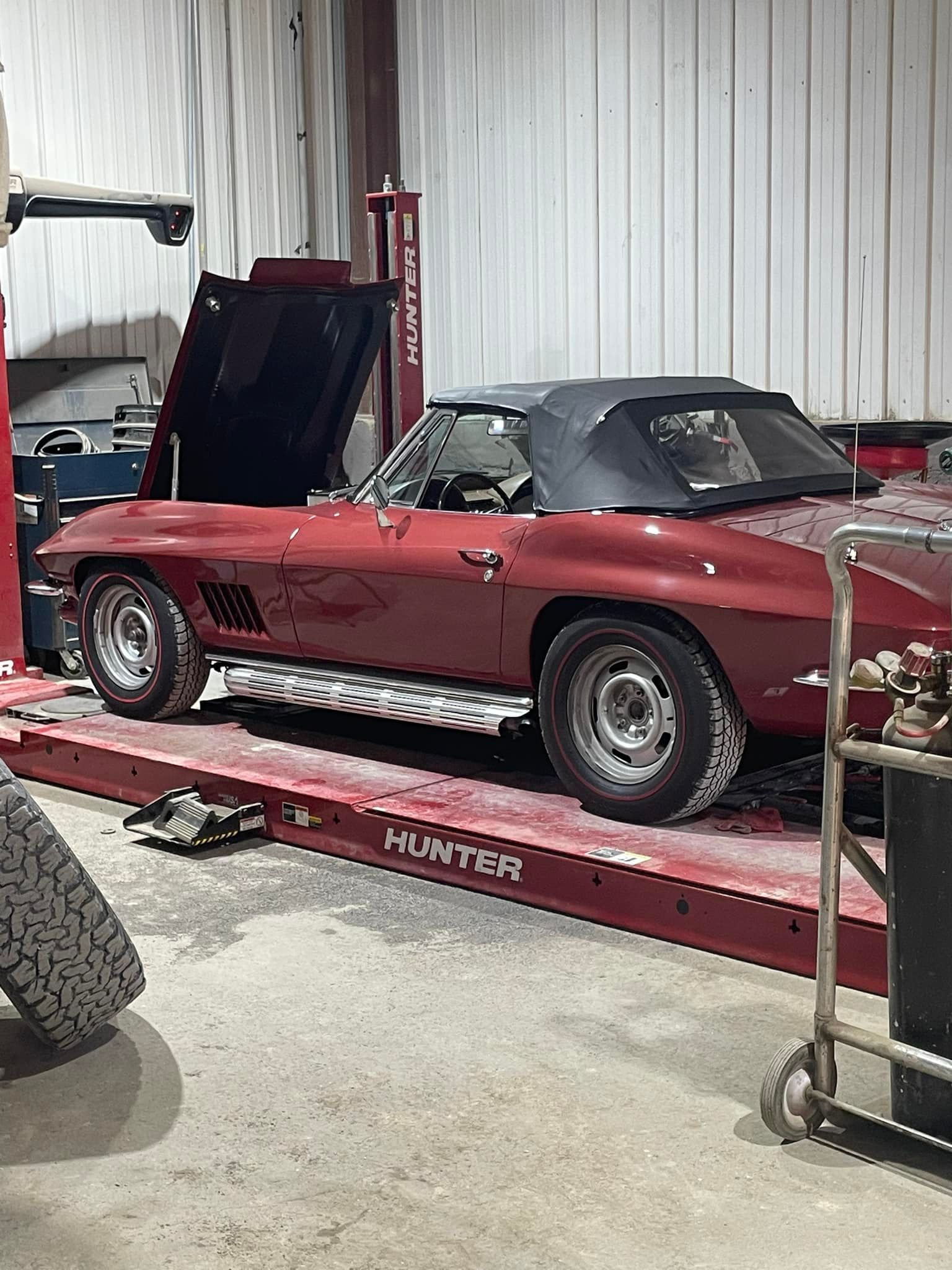 A red corvette is parked on a lift in a garage.