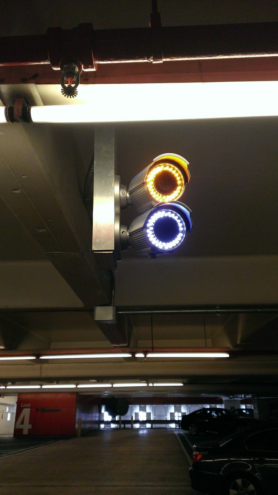 two security cameras are hanging from the ceiling of a parking garage .