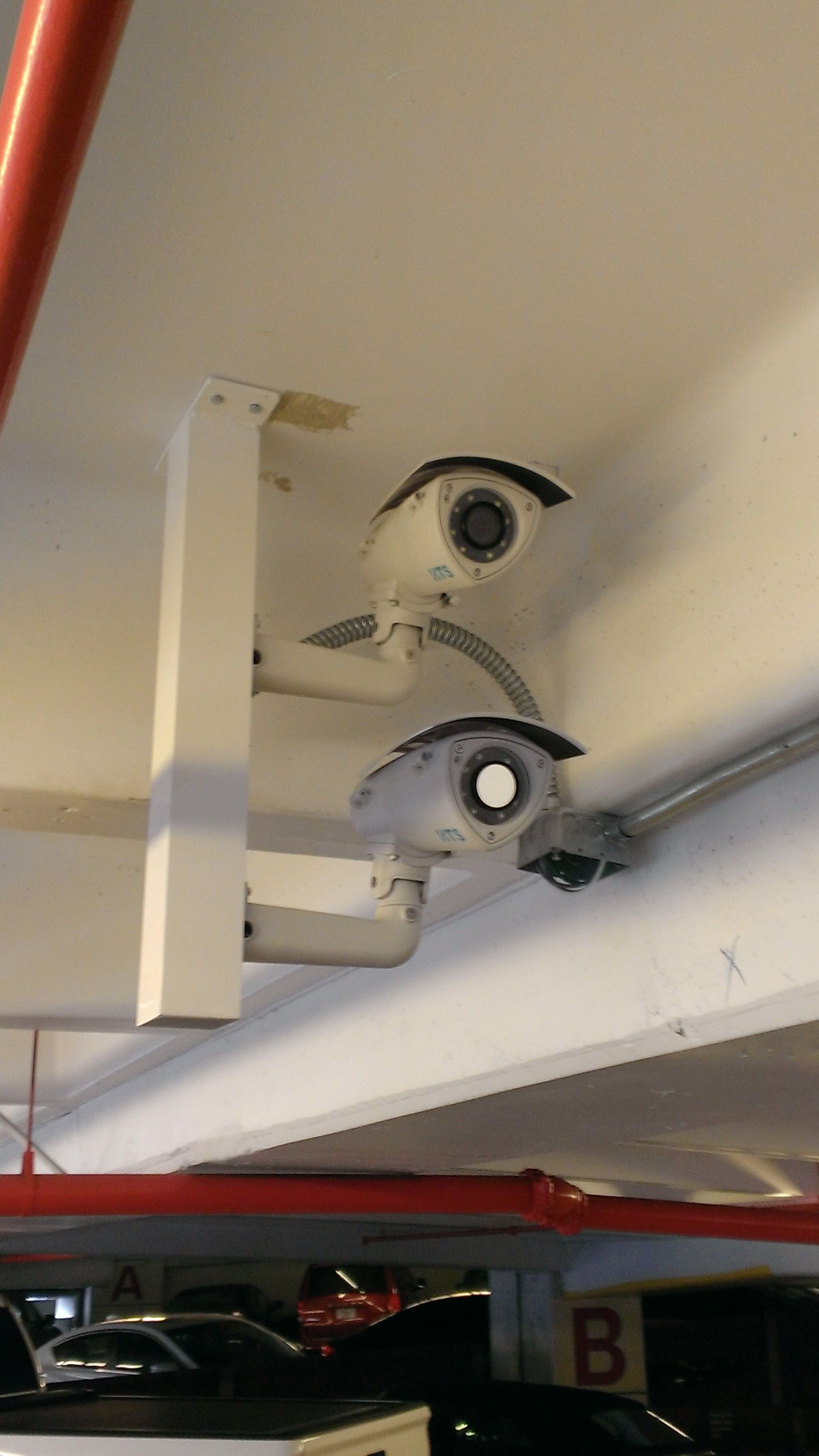 two security cameras are hanging from the ceiling of a parking garage .