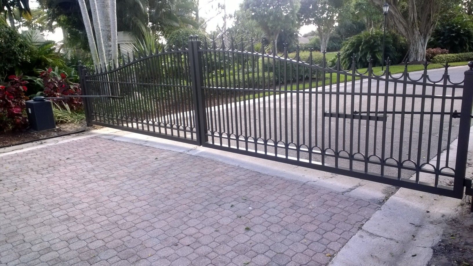 a black wrought iron gate is open to a driveway .