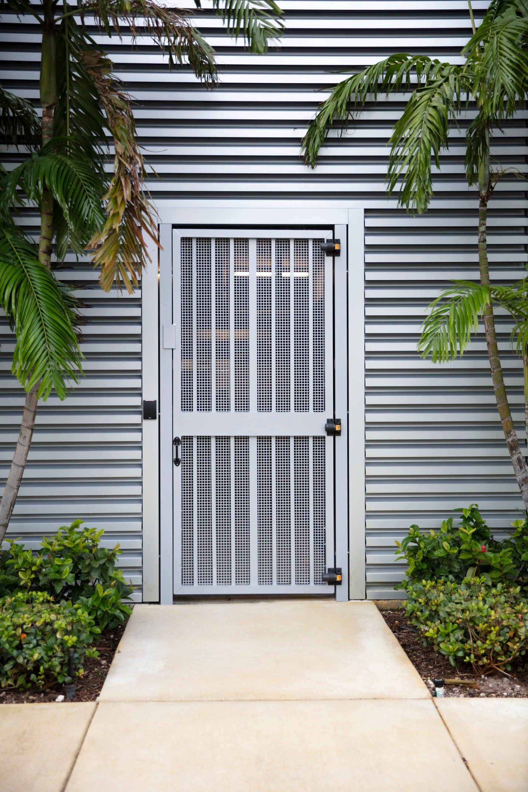 a metal door is surrounded by palm trees and a concrete walkway .