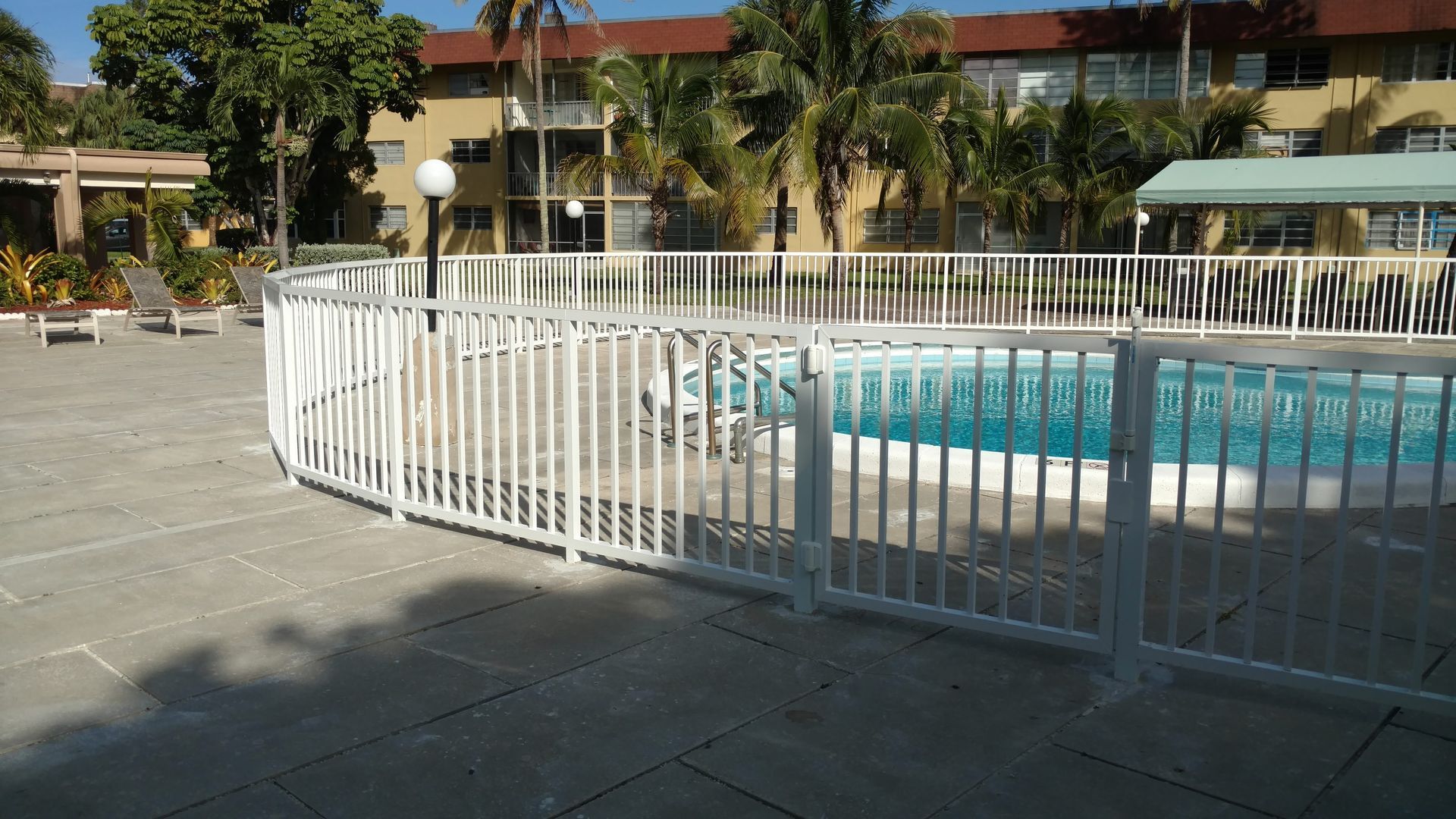 a white fence surrounds a swimming pool with a building in the background