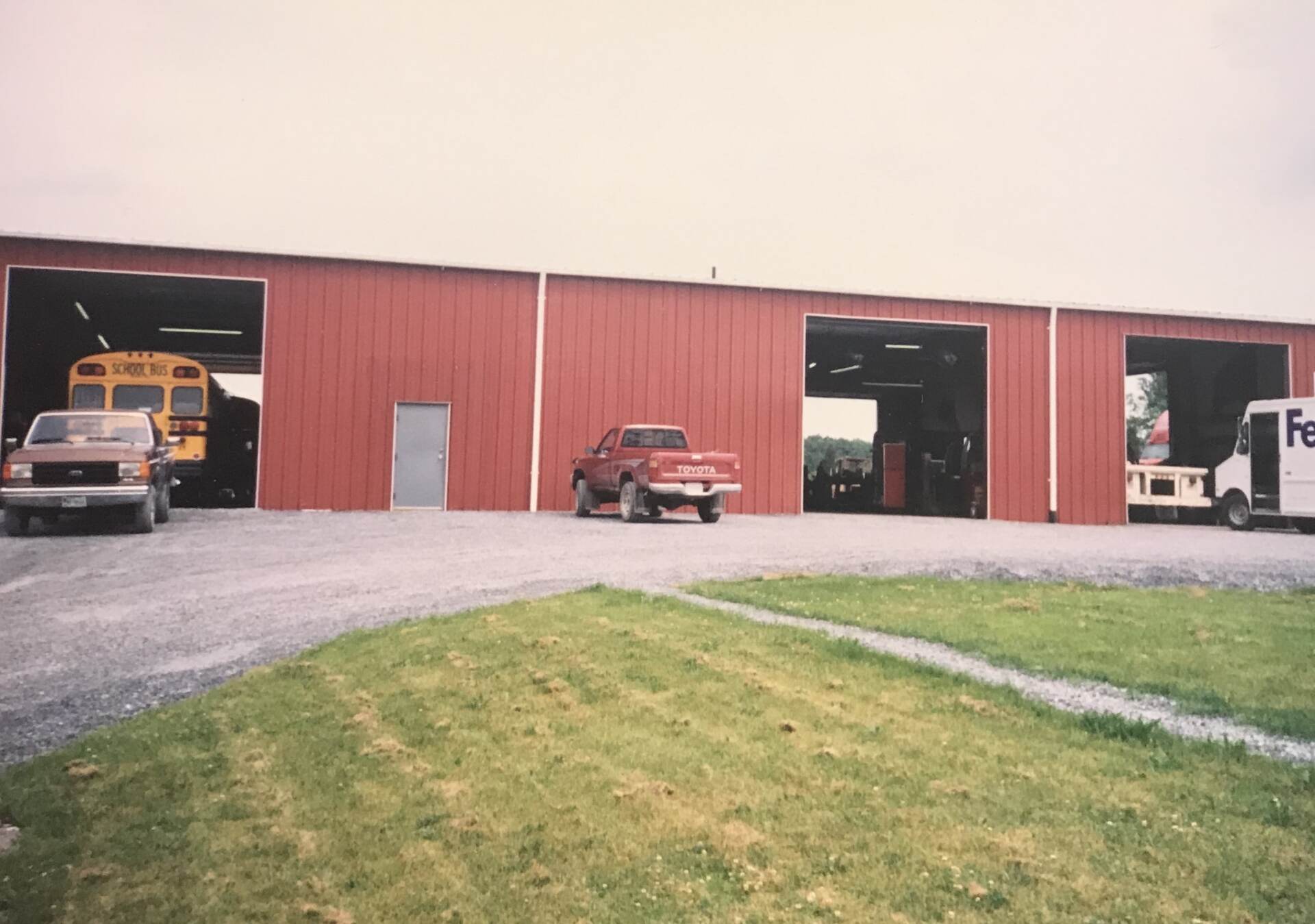 Red building with open bays, vehicles parked outside: school bus, truck, and FedEx van.