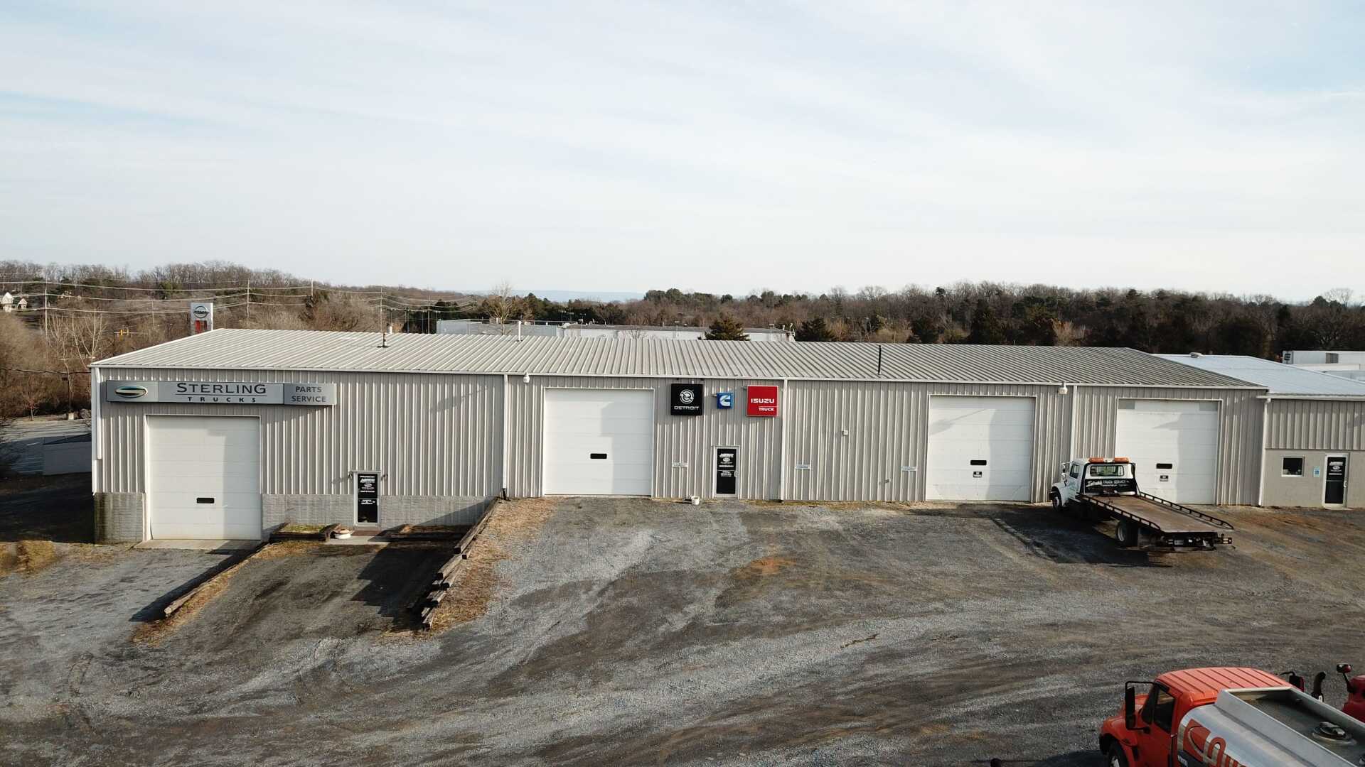 Warehouse building with white garage doors and signs, parked trucks, outdoor setting.