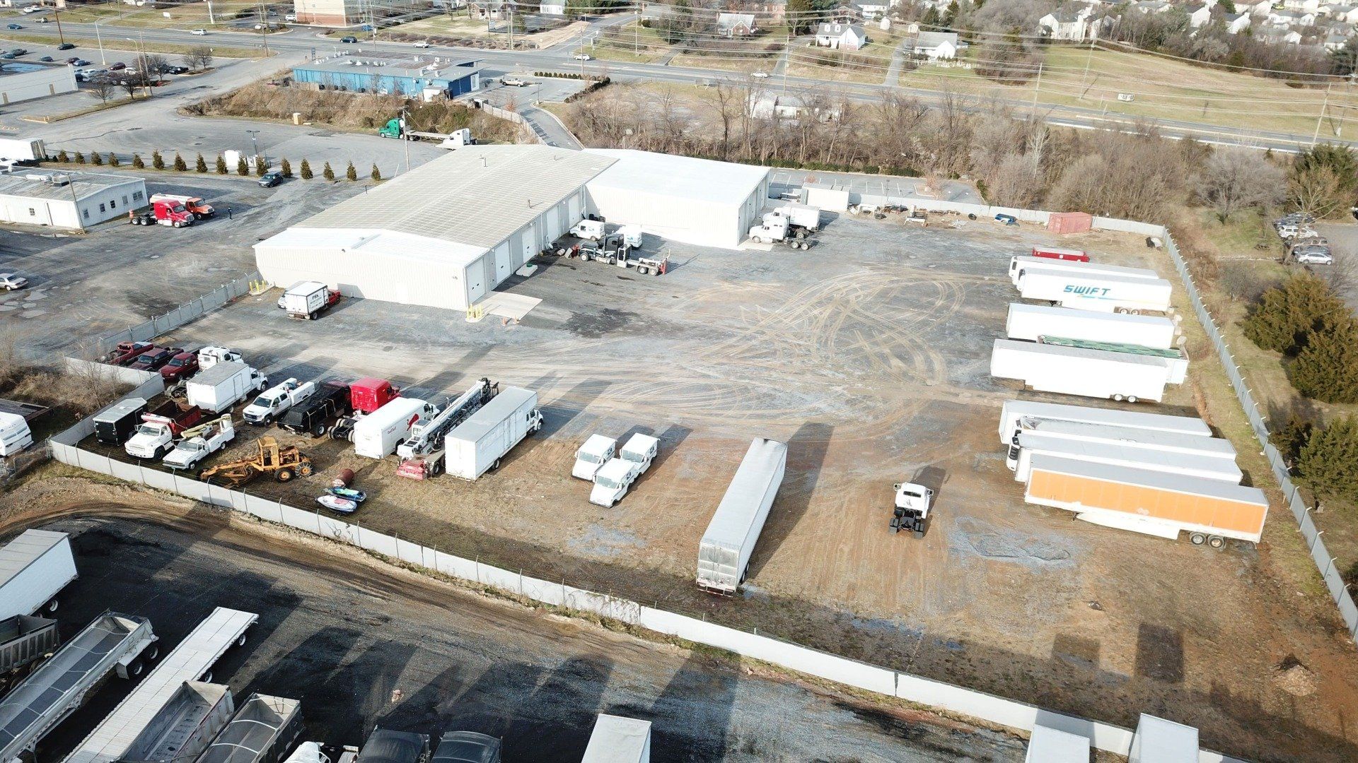 Aerial view of a commercial property with a large warehouse, trucks, trailers, and parked vehicles.