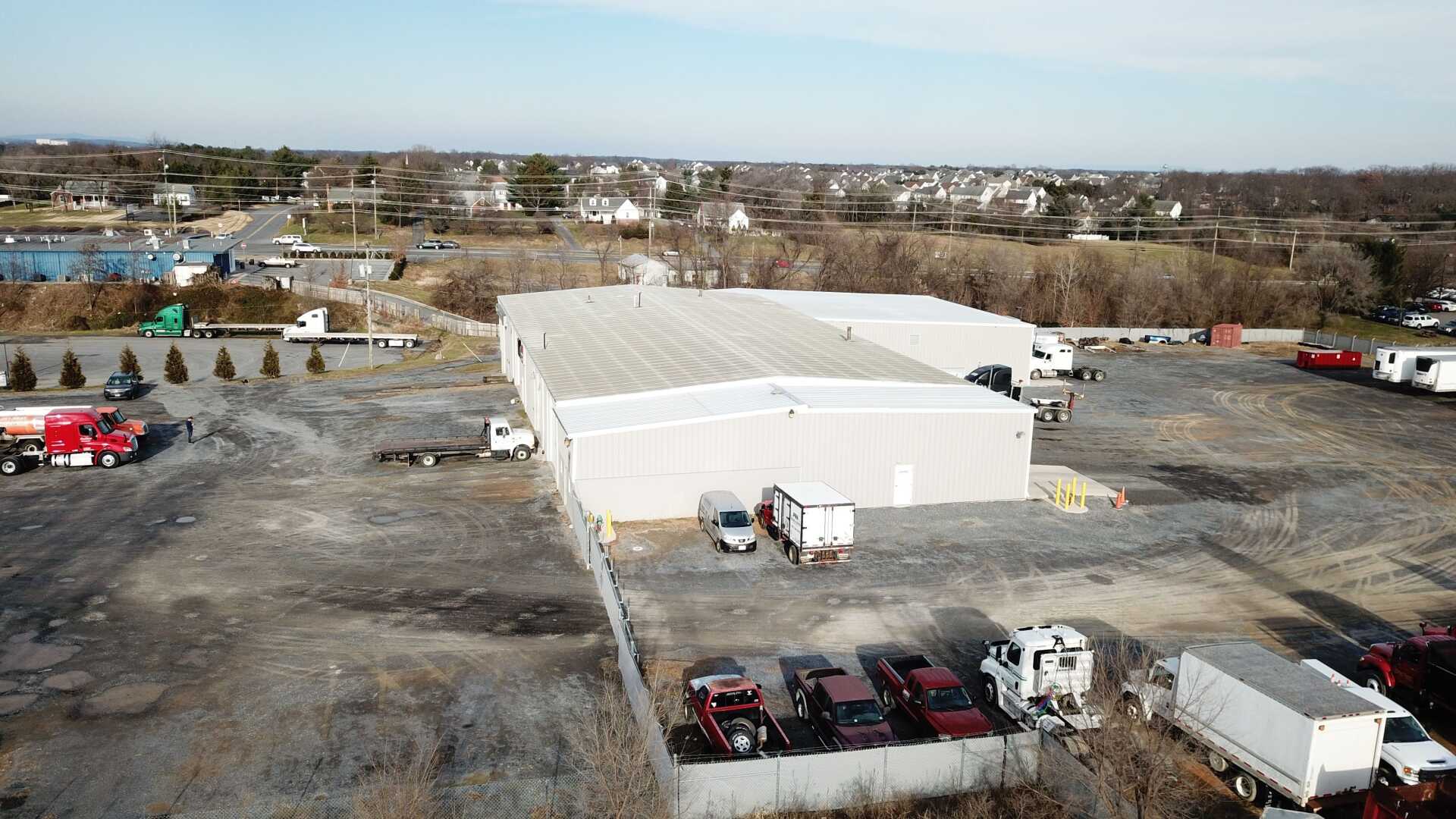 Aerial view of a commercial property with warehouses, trucks, and parked vehicles on a gravel lot.