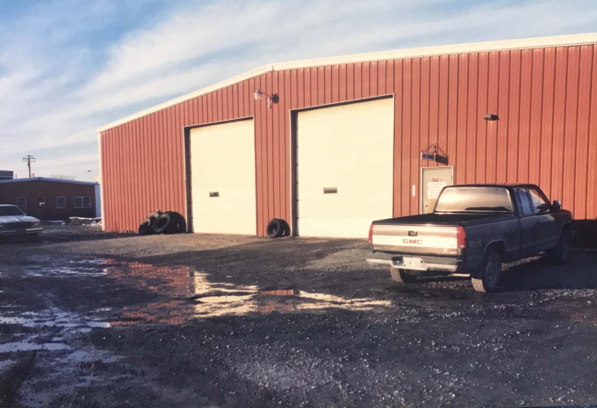 Red metal building with two garage doors, parked truck in gravel lot.
