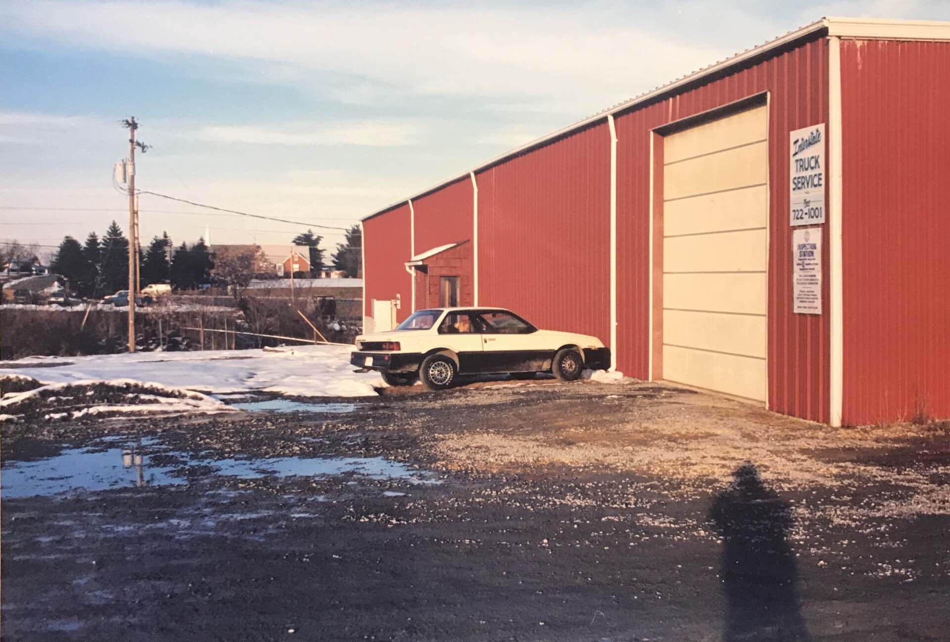 A red building with a garage door, a car outside, and snow on the ground.