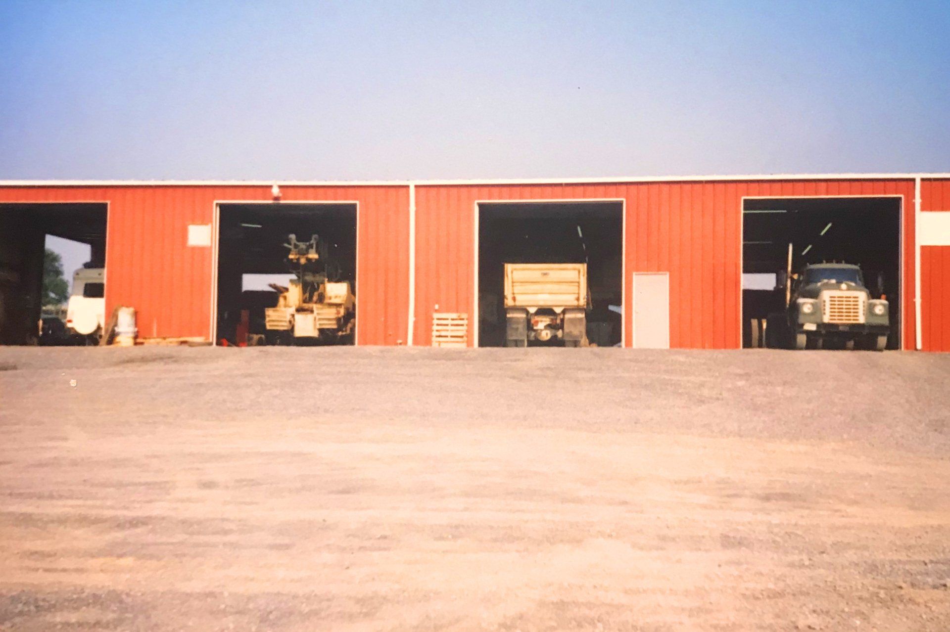 Red garage bays with heavy machinery inside, parked on gravel.