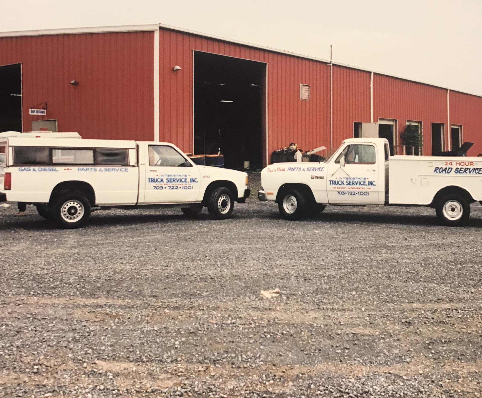 Two white pickup trucks parked in front of a red building, both with the same company logo.