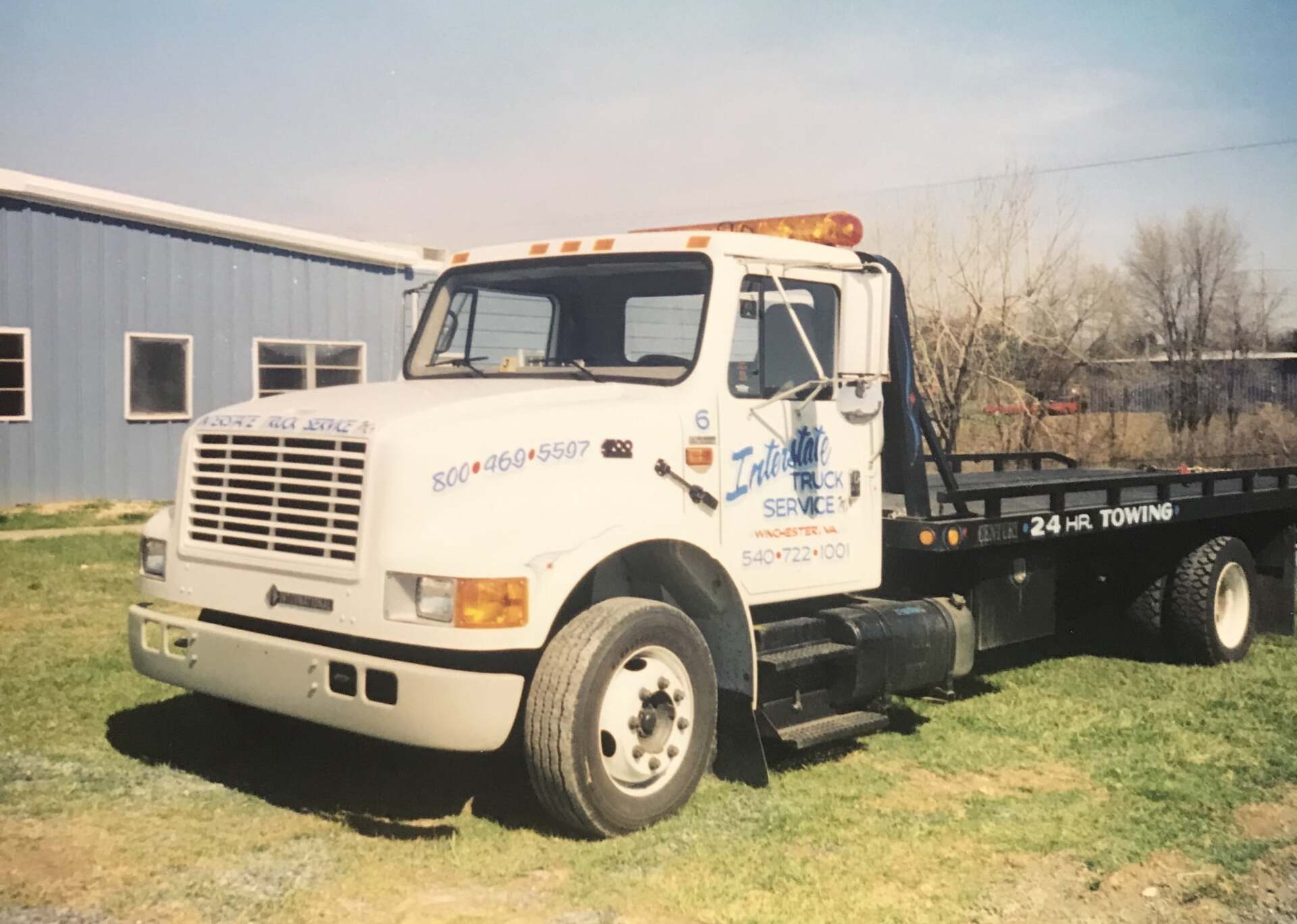 White tow truck on green grass; parked in front of a blue building.