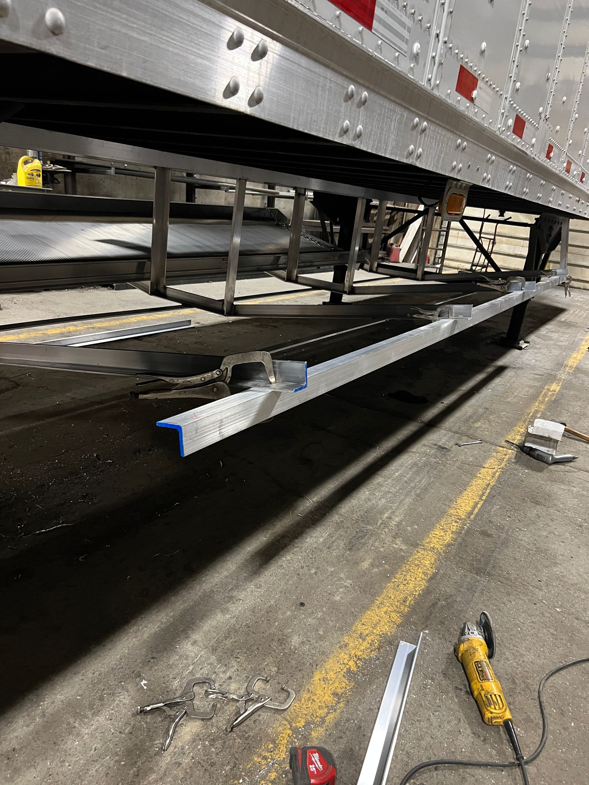 A low angle view of a trailer’s undercarriage with metal being cut and worked on near a concrete floor.