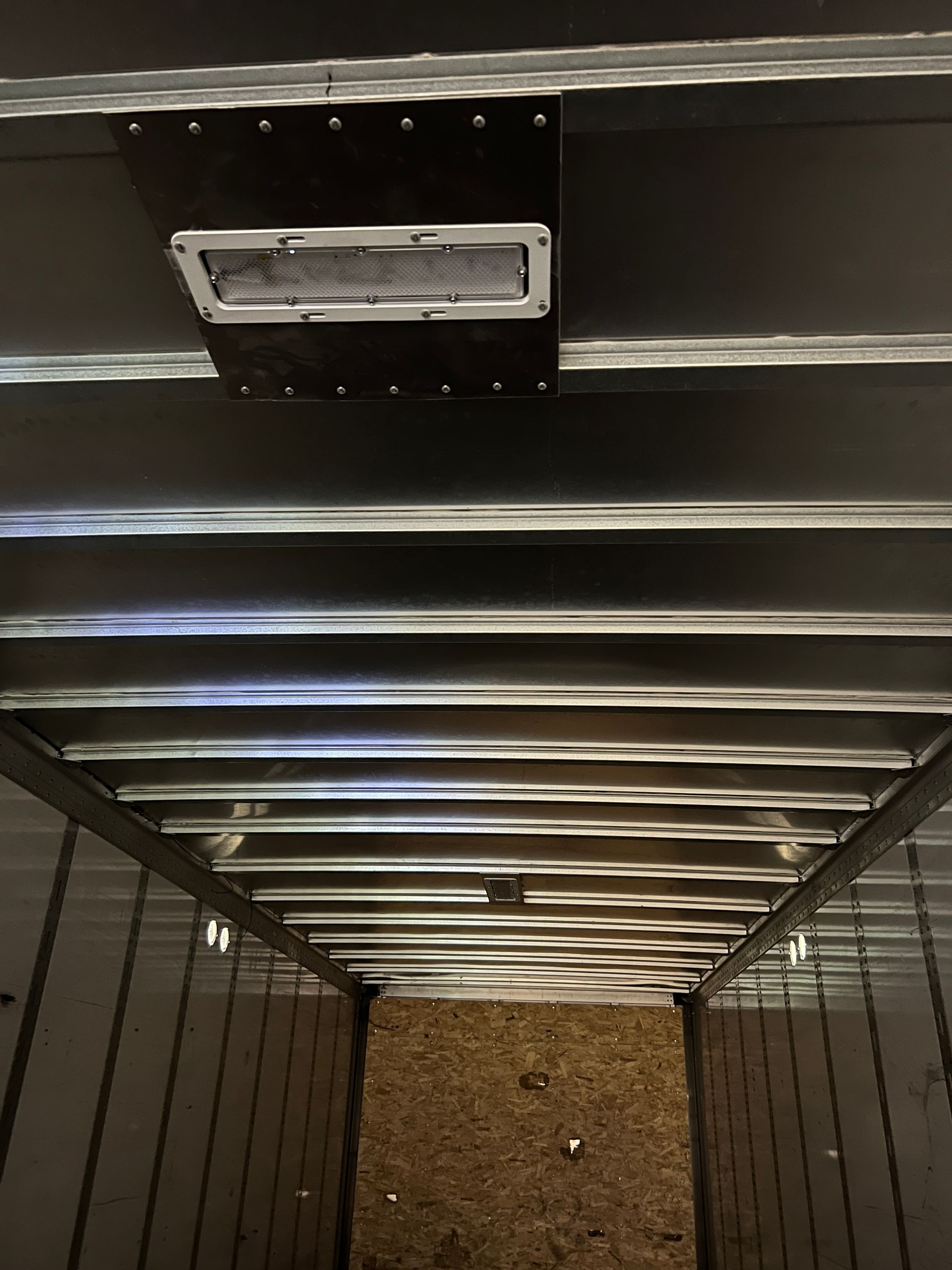 Inside a cargo trailer; rectangular light fixture mounted on ceiling with wooden floor visible below.