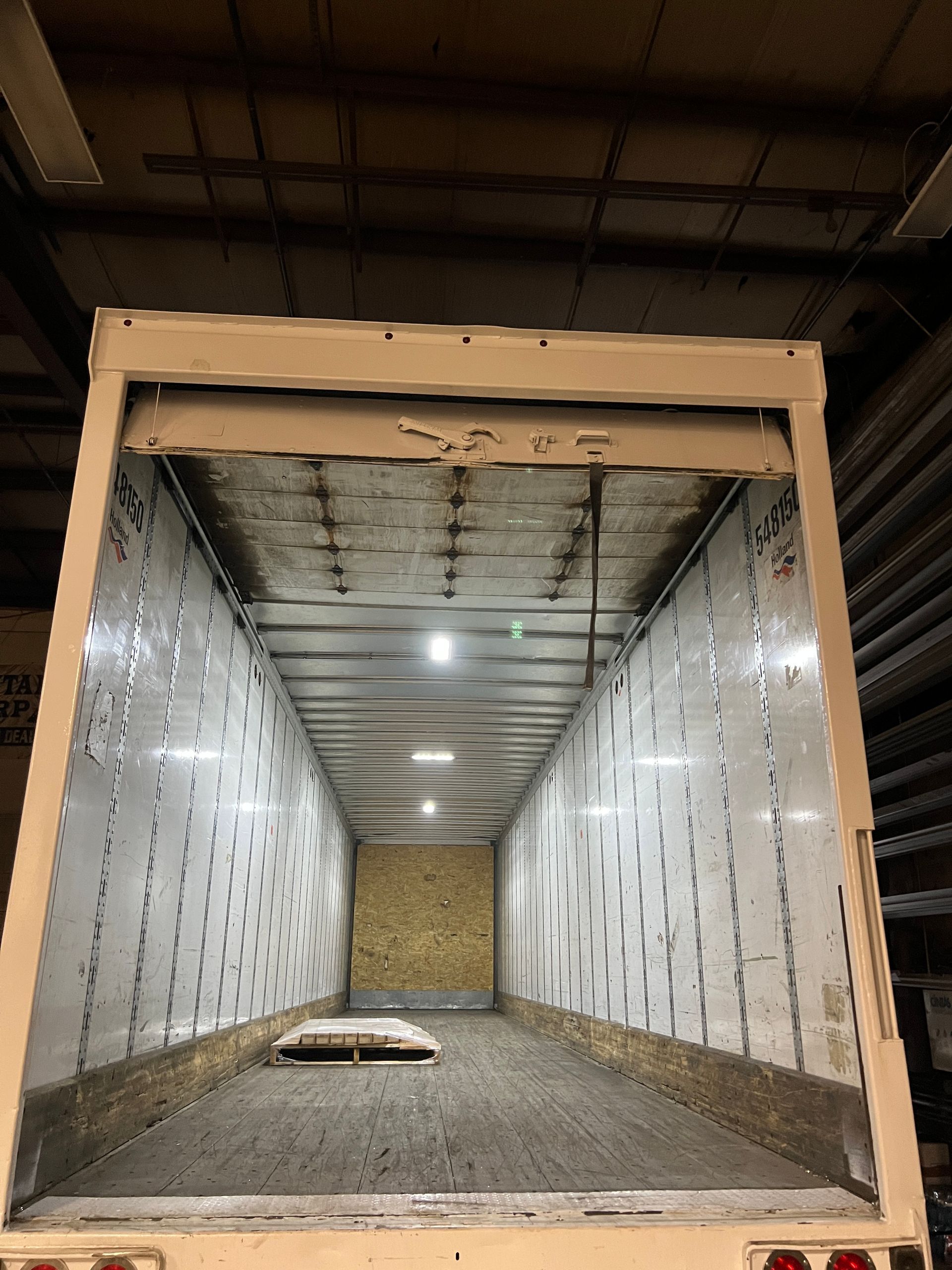 Empty white truck trailer interior with lights, showing floor and walls.