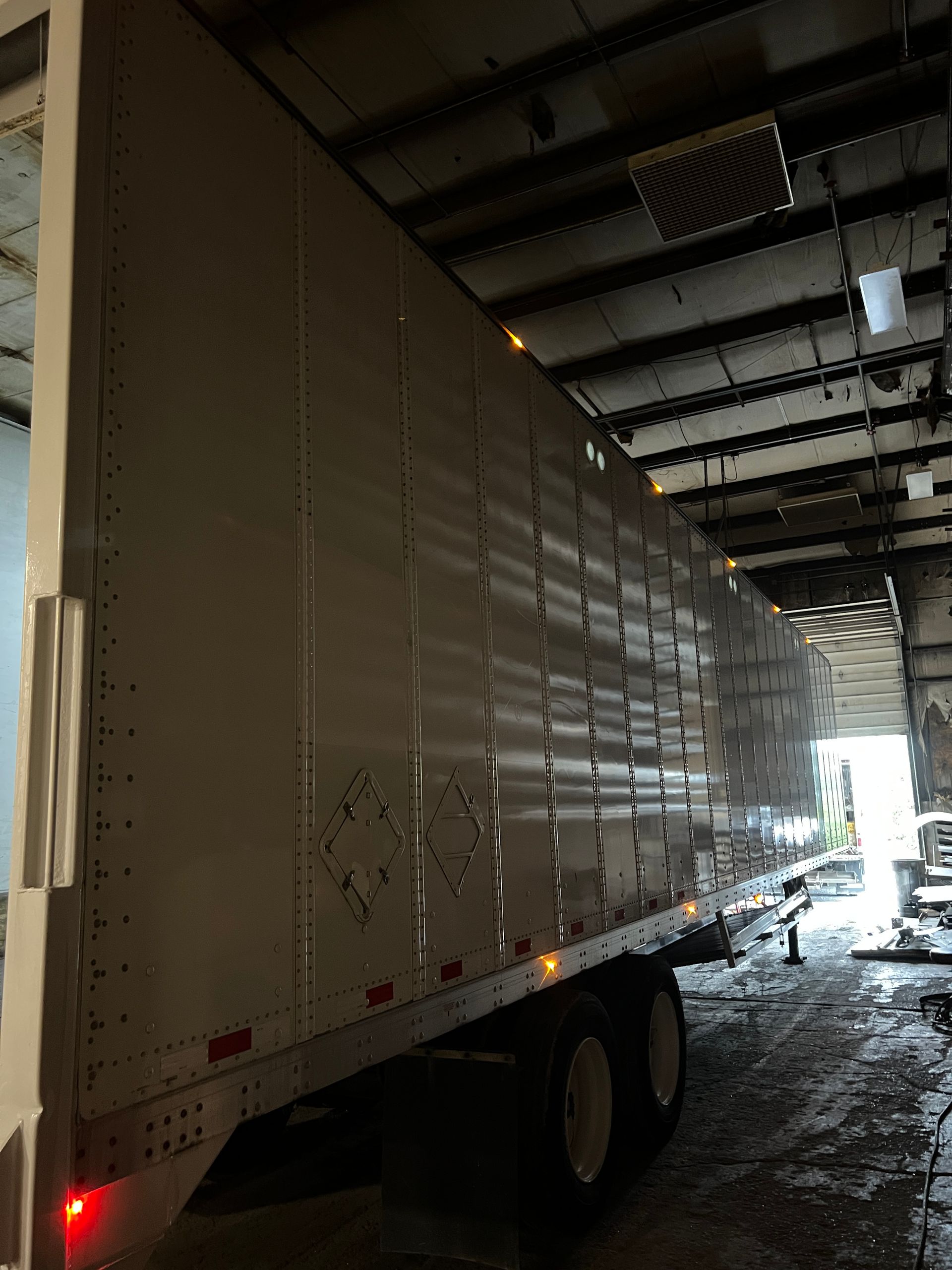 White semi-trailer in a dimly lit warehouse. Doors are open, revealing a glimpse of the outside.