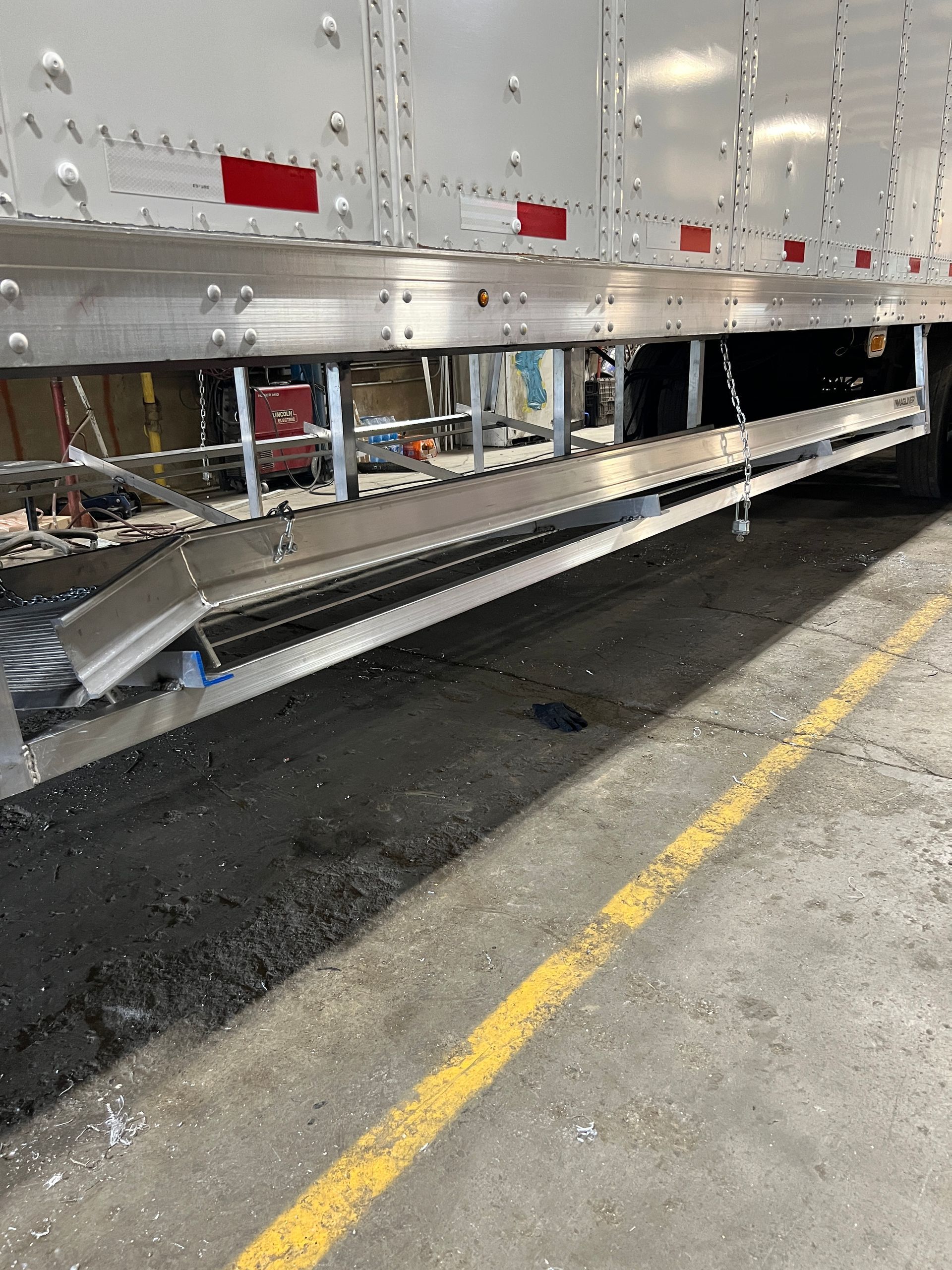 A metal ramp extending from a truck trailer on a concrete floor with yellow line.