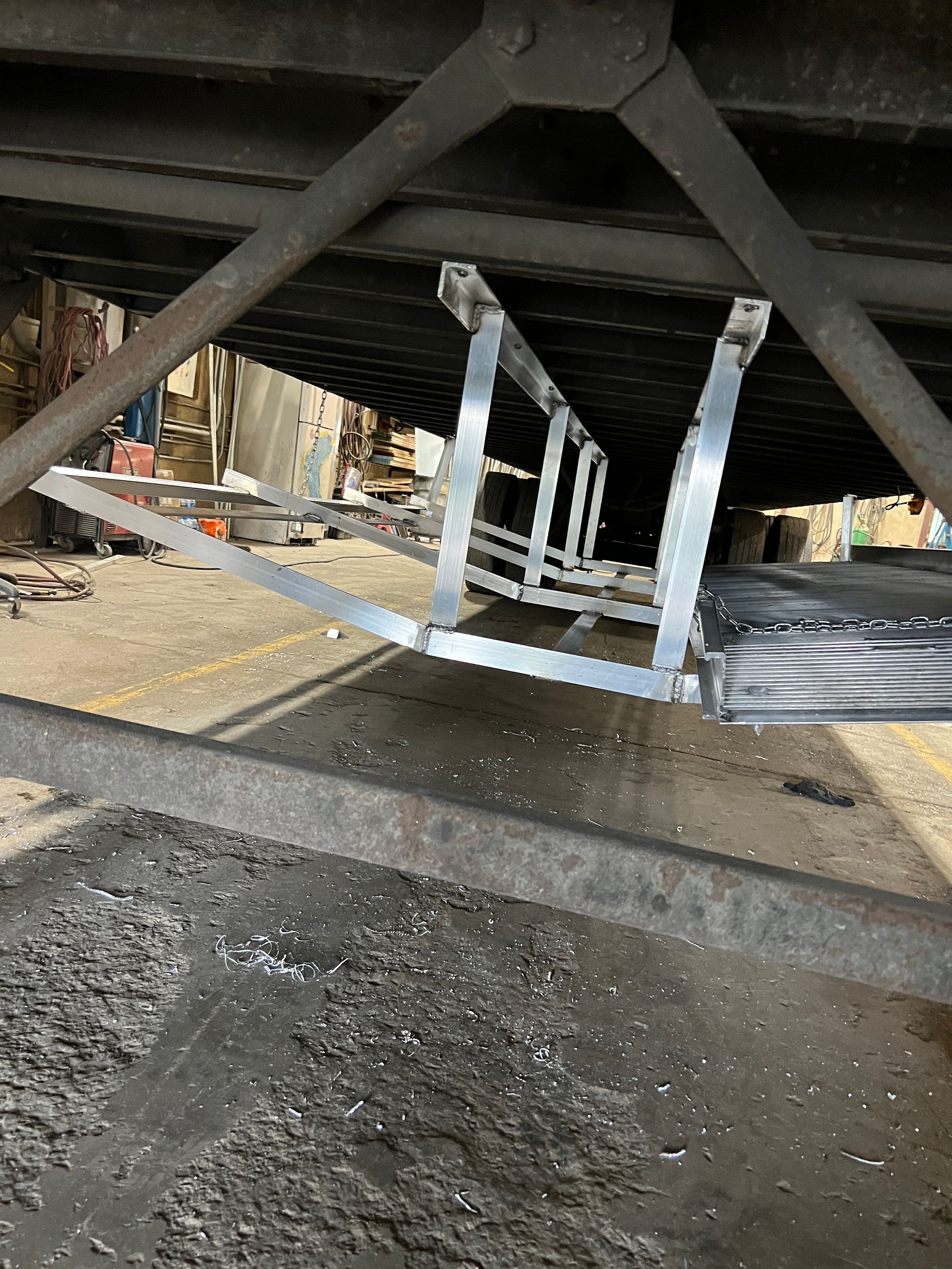 Underneath a truck trailer: metallic ladder-like structure with a road surface beneath.