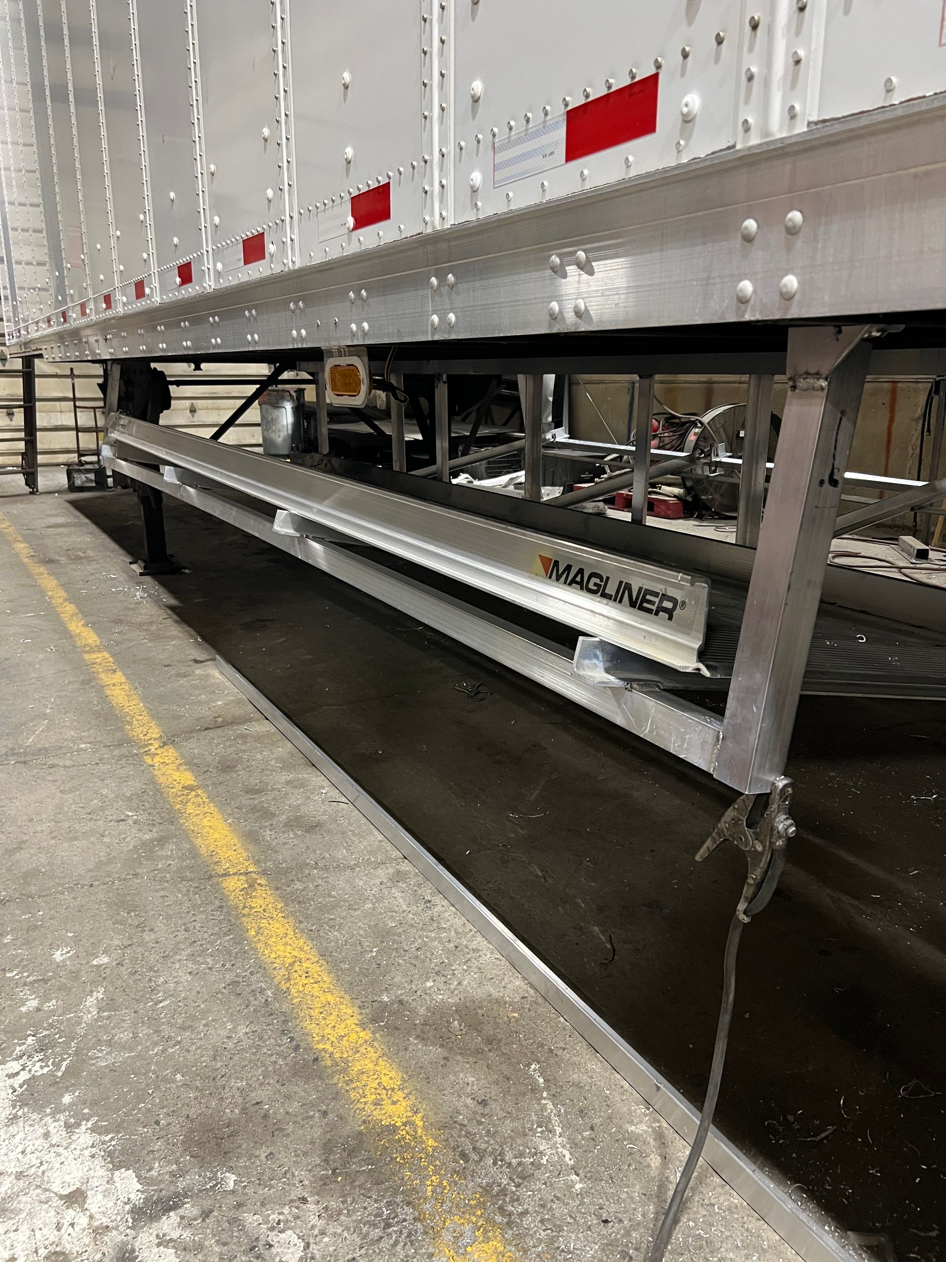 Side view of a white semi-trailer with a retractable ramp, possibly for loading/unloading freight.