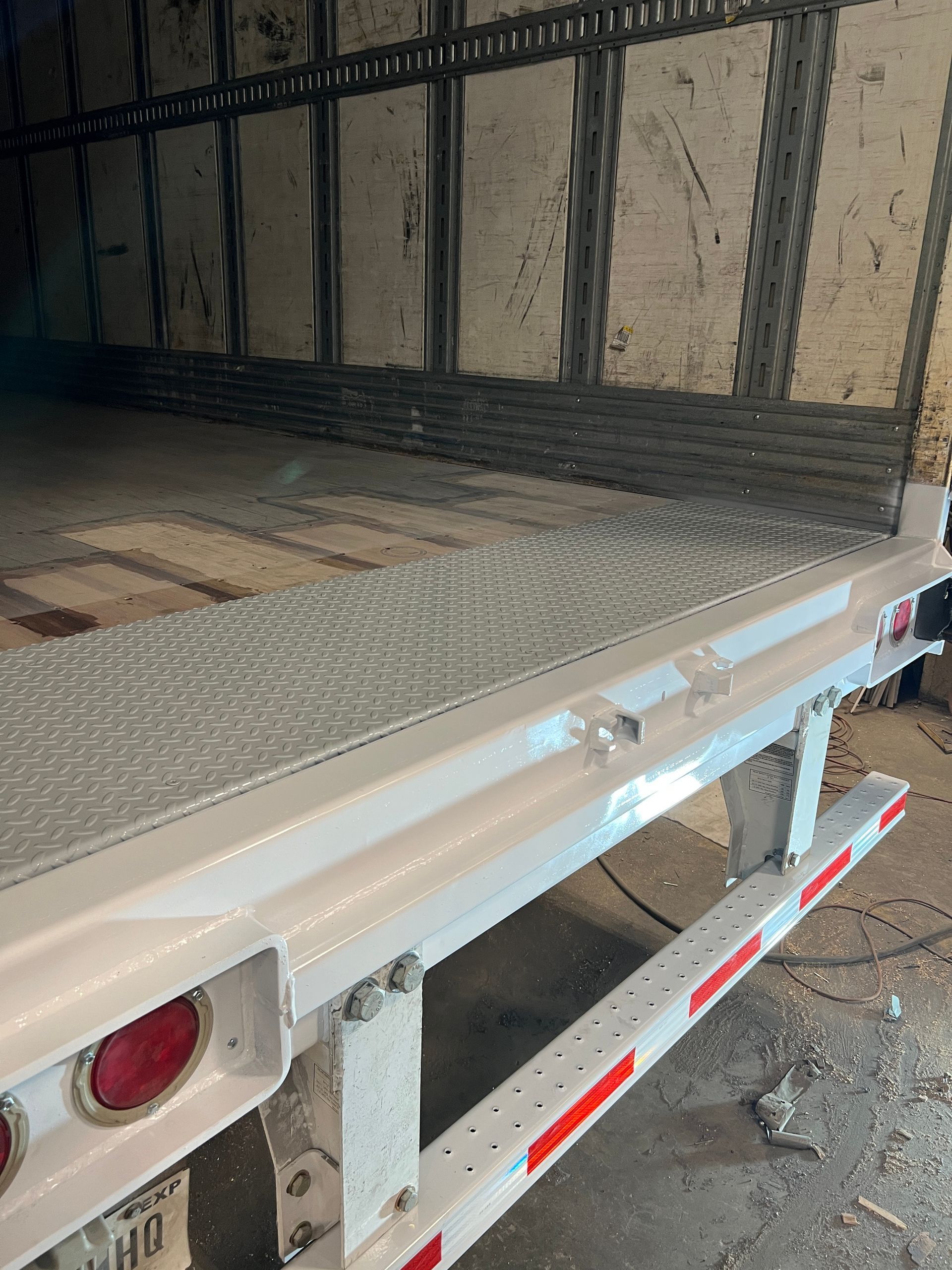 A white truck is parked in a garage with the back door open.