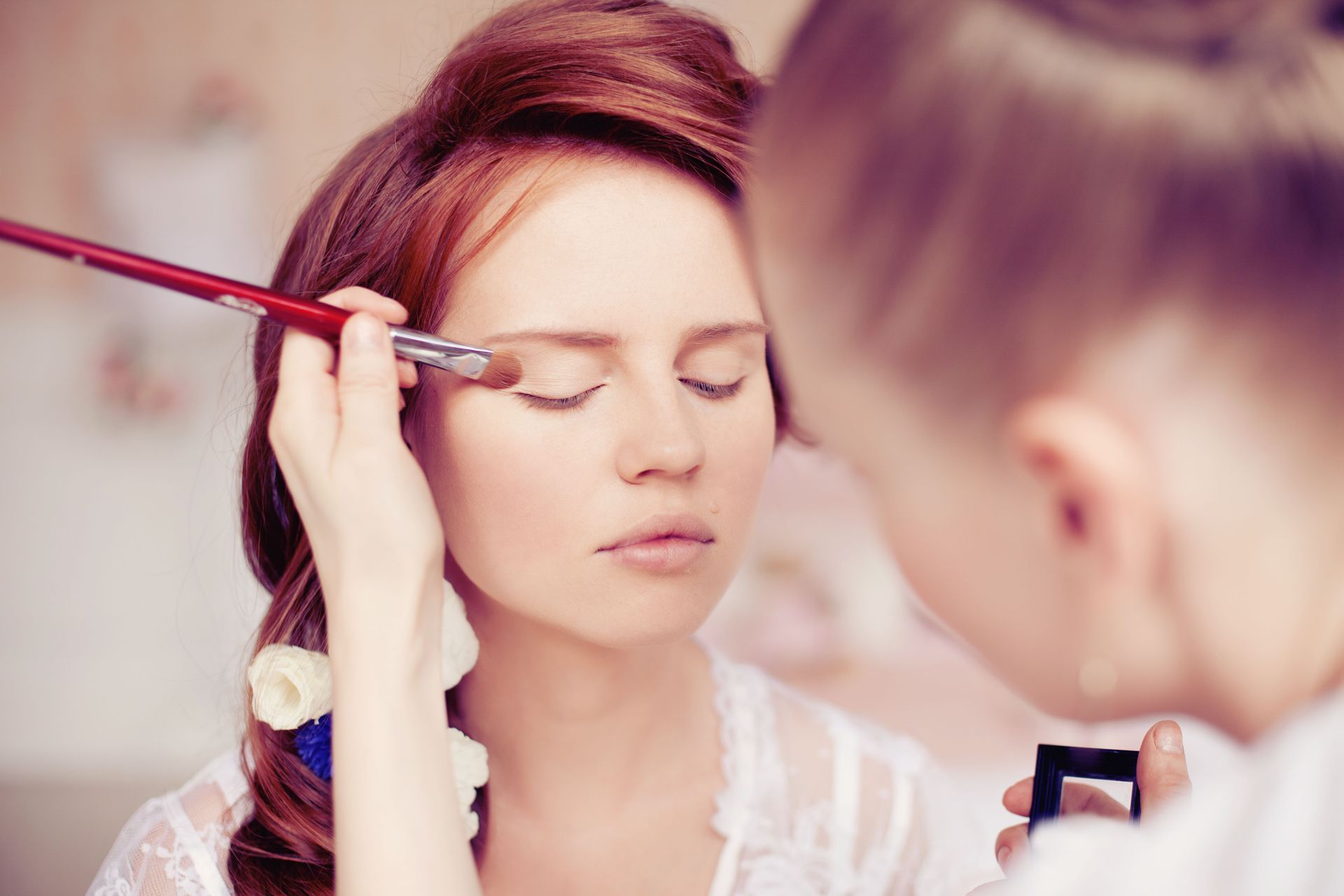 Makeup artist applying eyeshadow to a woman's closed eyelid with a brush.