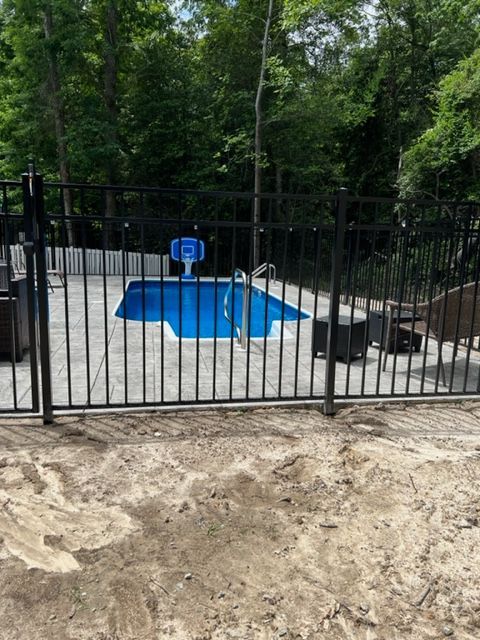 A fence surrounds a swimming pool with a basketball hoop in the background.