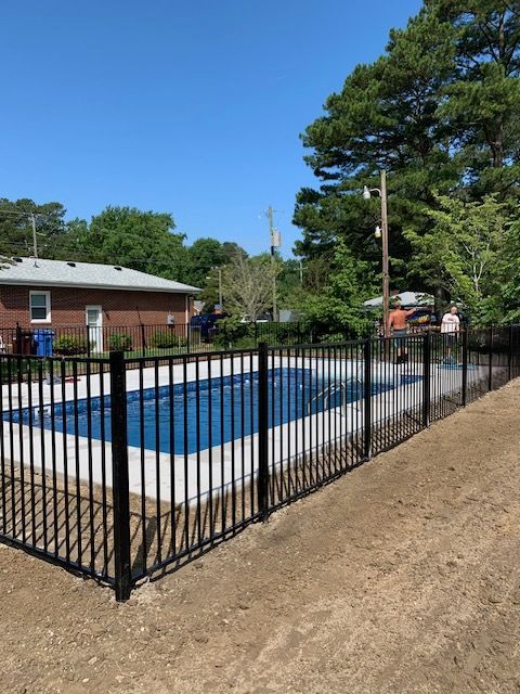 A black fence surrounds a swimming pool in front of a house