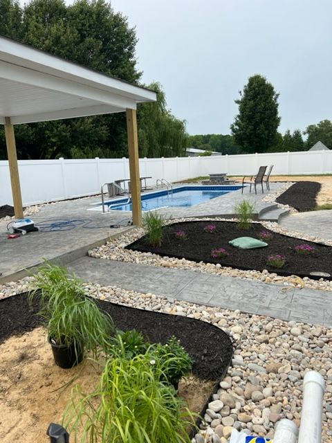 A swimming pool is surrounded by rocks and plants in a backyard.