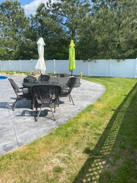 A patio with a table and chairs and umbrellas in a backyard.
