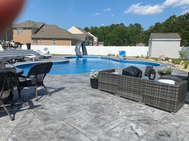 A large swimming pool is surrounded by patio furniture and chairs.