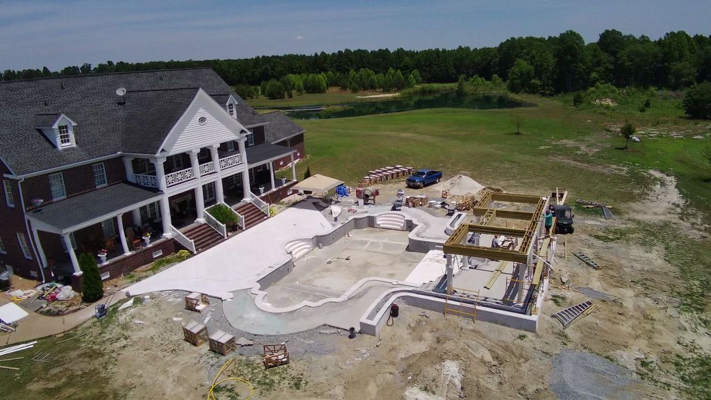 An aerial view of a large house under construction with a large pool in the backyard.