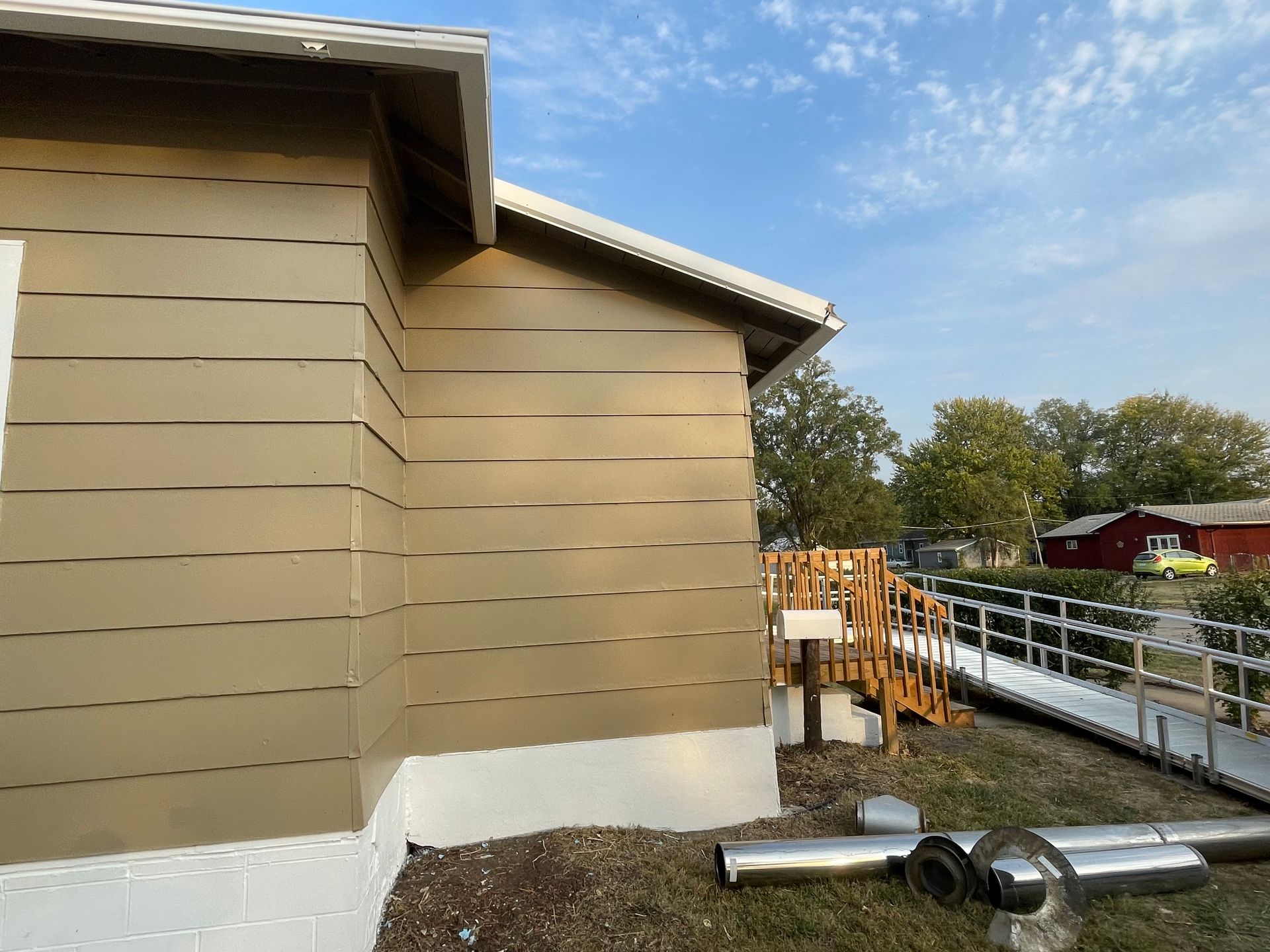 Tan-sided building with white trim, near a ramp and trees under a partly cloudy sky.