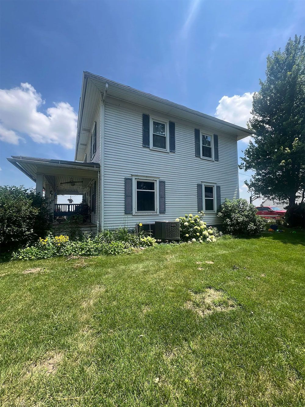 Two-story white house with blue shutters, covered porch, and green lawn under a sunny blue sky.